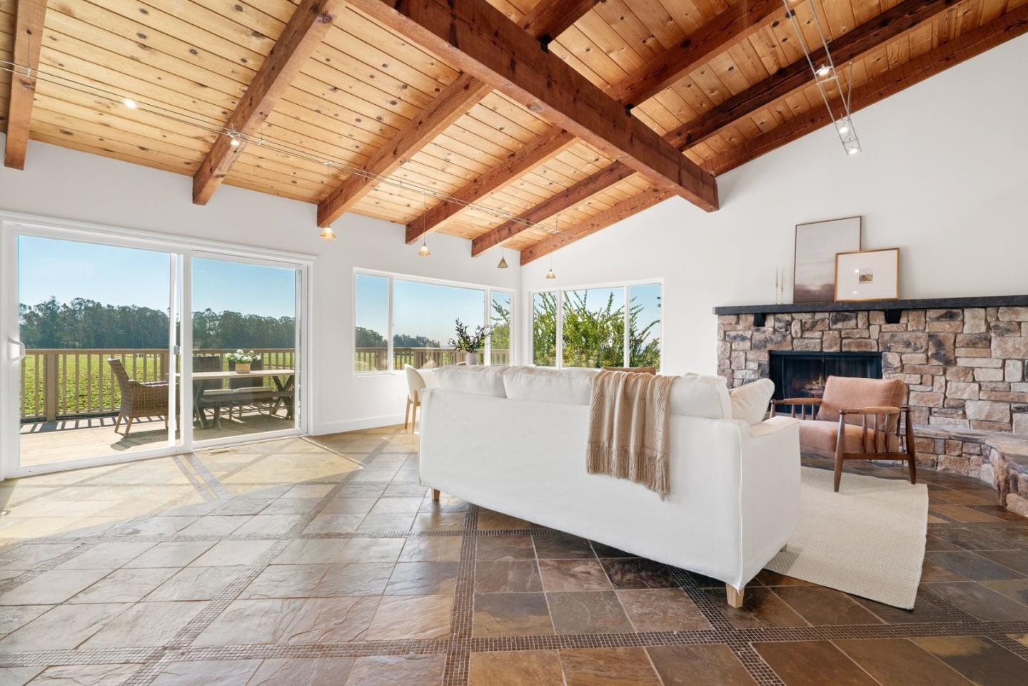 Living room with a vaulted wood-beam ceiling, stone fireplace, and glass doors to a deck.