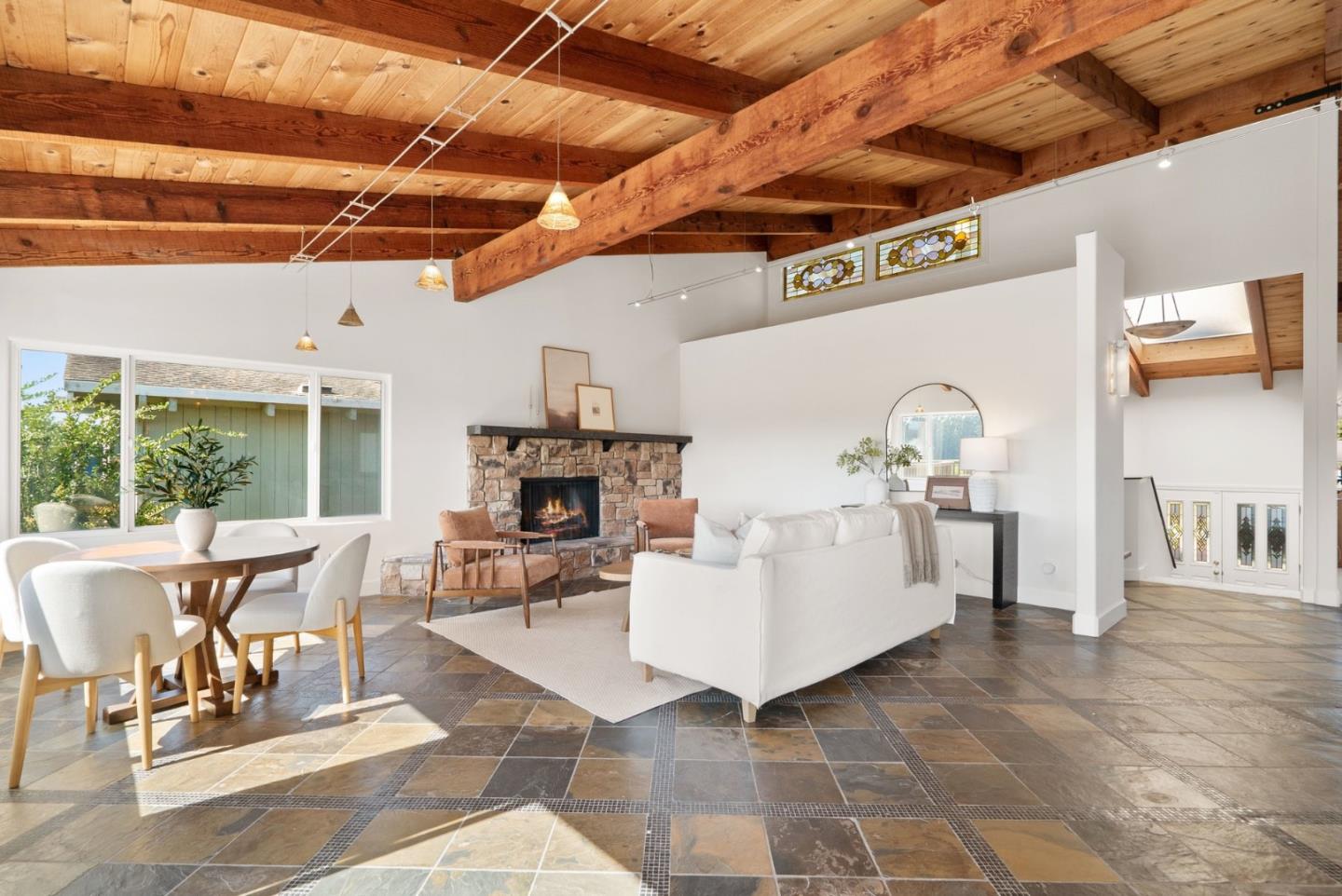 Living room with exposed timber beams, stone fireplace, and adjoining dining area.