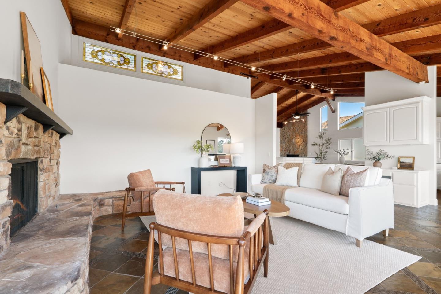 Living room with a stone fireplace, white sectional, and exposed timber ceiling beams.