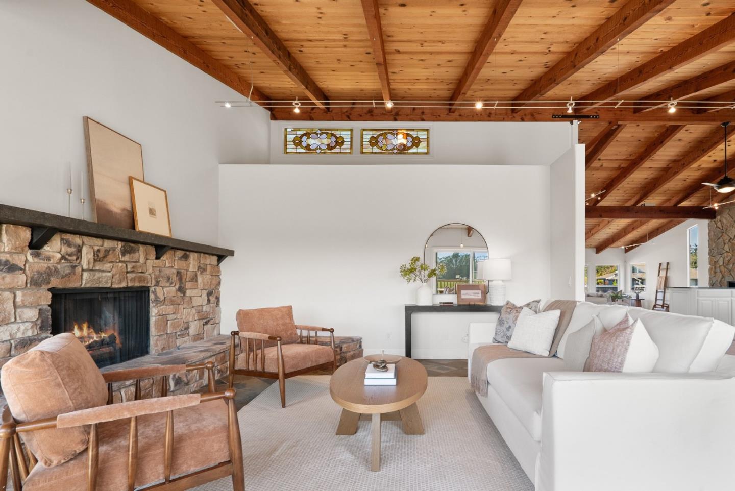 Living room with a stone fireplace, exposed wood ceiling, and white sofa with leather chairs.
