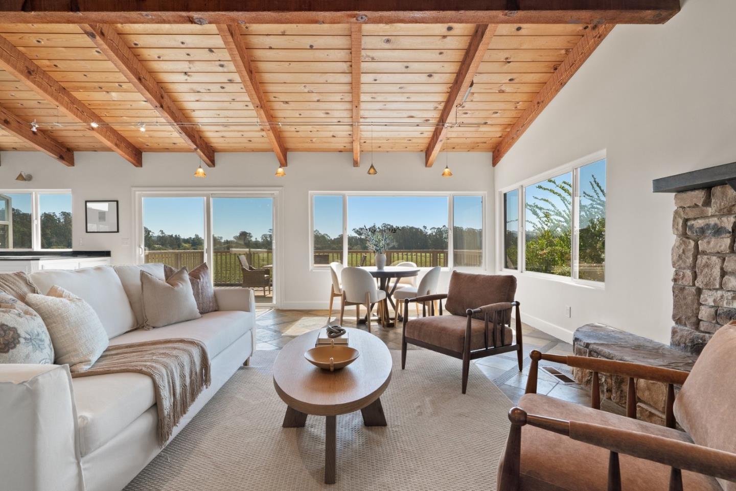 Living room with exposed timber ceiling, stone fireplace, and windows overlooking trees.