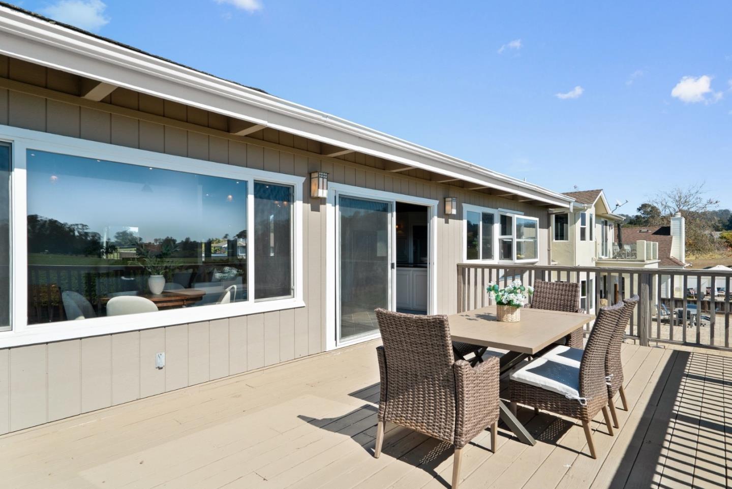 Furnished deck with a wicker dining set beside large windows and sliding glass doors.