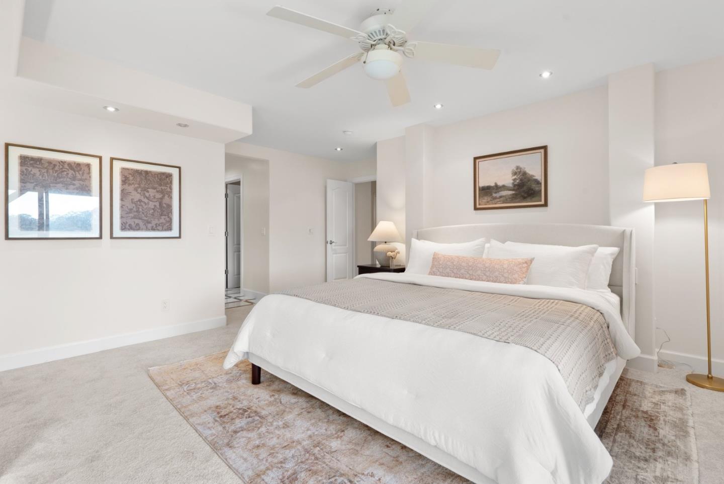 Bright bedroom with a large white bed, ceiling fan, and framed wall art.