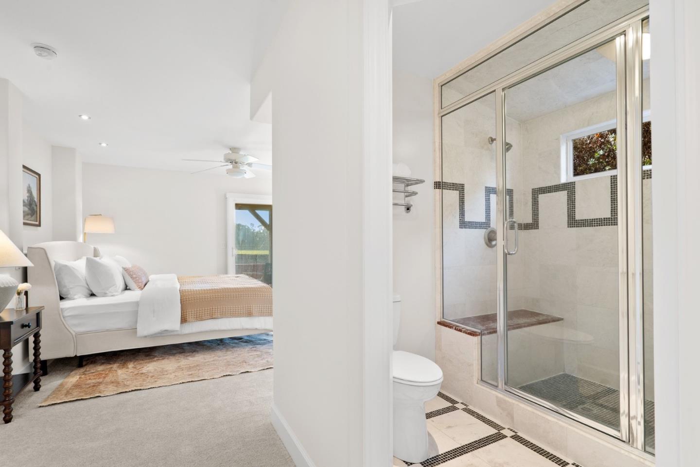Staged bedroom beside an ensuite bathroom with a glass shower and tiled bench.