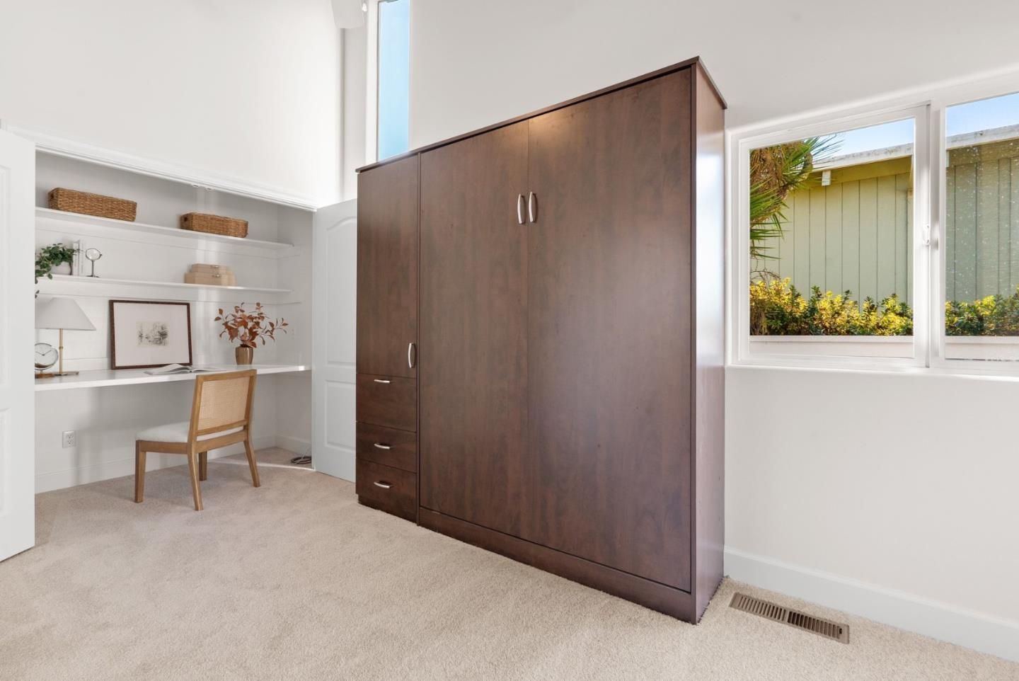 Bright home office with a built-in desk, display shelves, and a large dark wood cabinet.