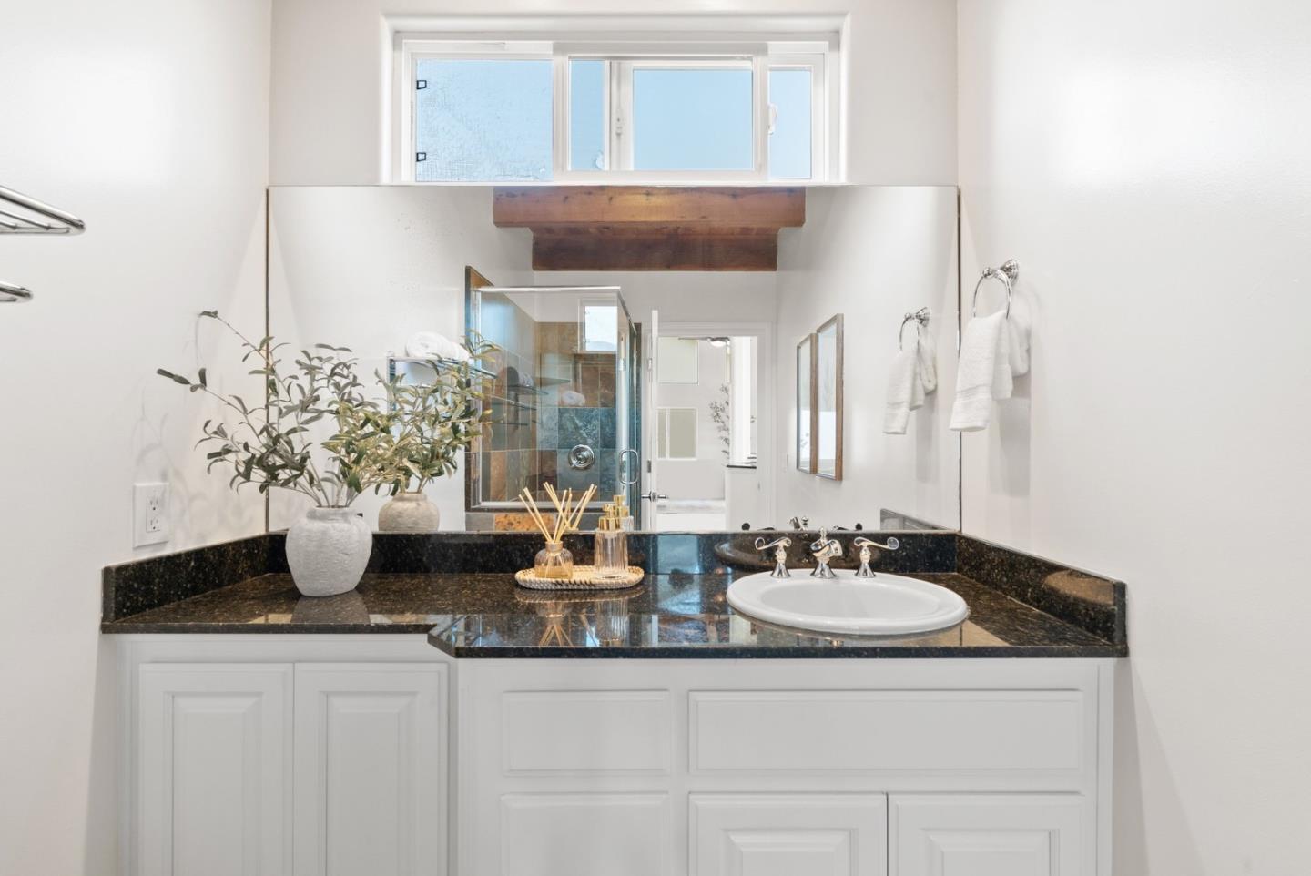 Bathroom vanity with dark granite countertop, oval sink, large mirror, and high window.