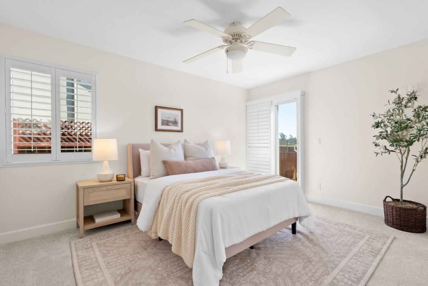 Bedroom with a white bed, shuttered windows, ceiling fan, and potted tree.