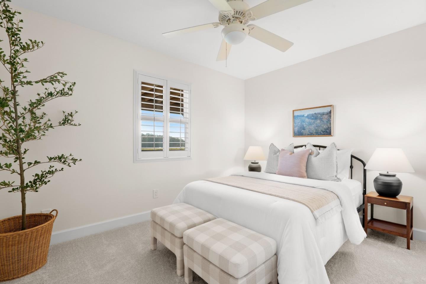 Bright bedroom with a white bed, shuttered window, and two checkered benches at the foot.