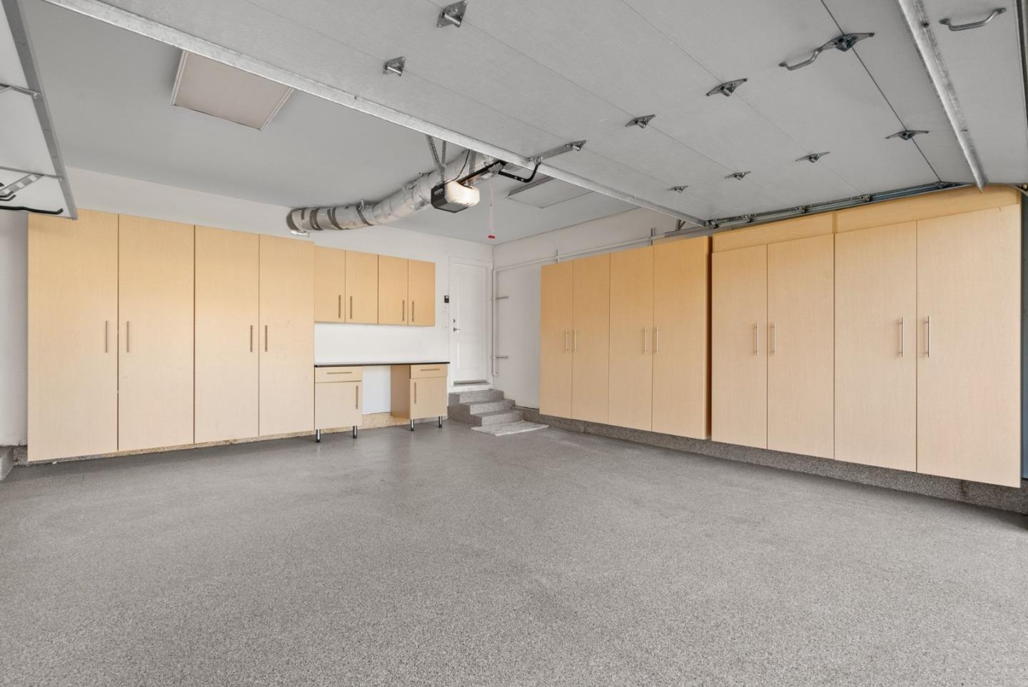 Empty garage with light-wood storage cabinets, a small work counter, and a gray floor.