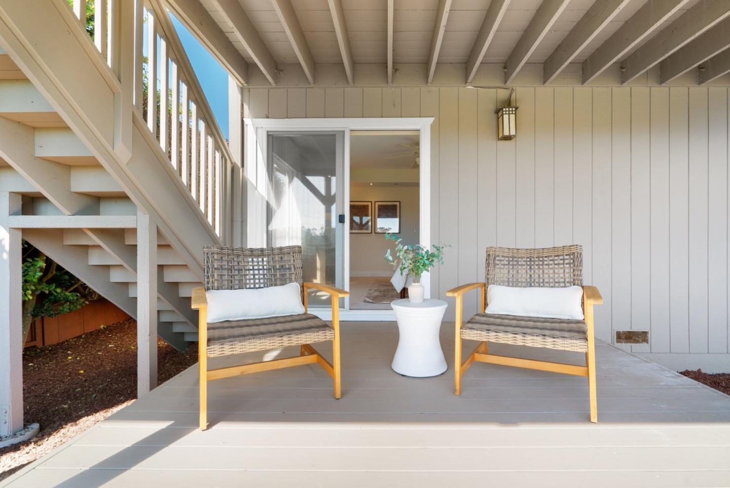 Covered patio with wicker chairs, a small table, and exterior stairs beside a sliding glass door.
