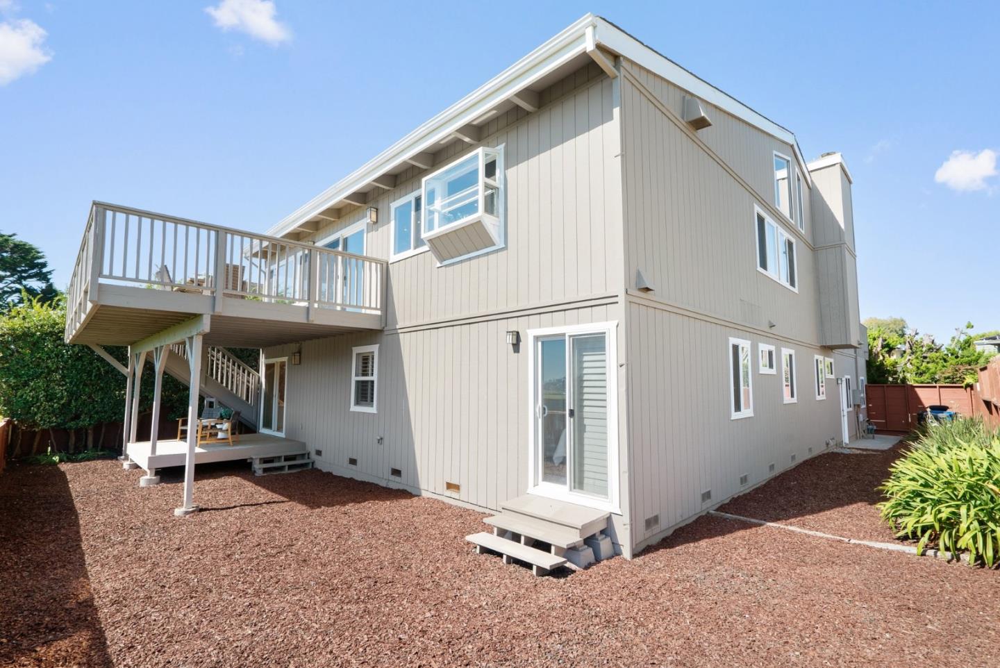 Two-story gray home with an elevated deck, exterior stairs, and a bark-mulch yard.