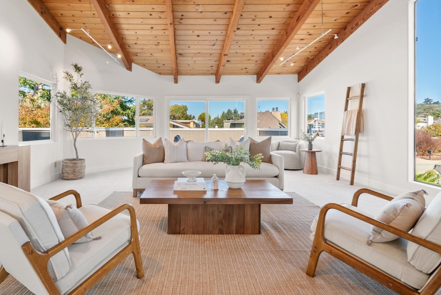 Living room with an exposed wood ceiling, large windows, and neutral seating.