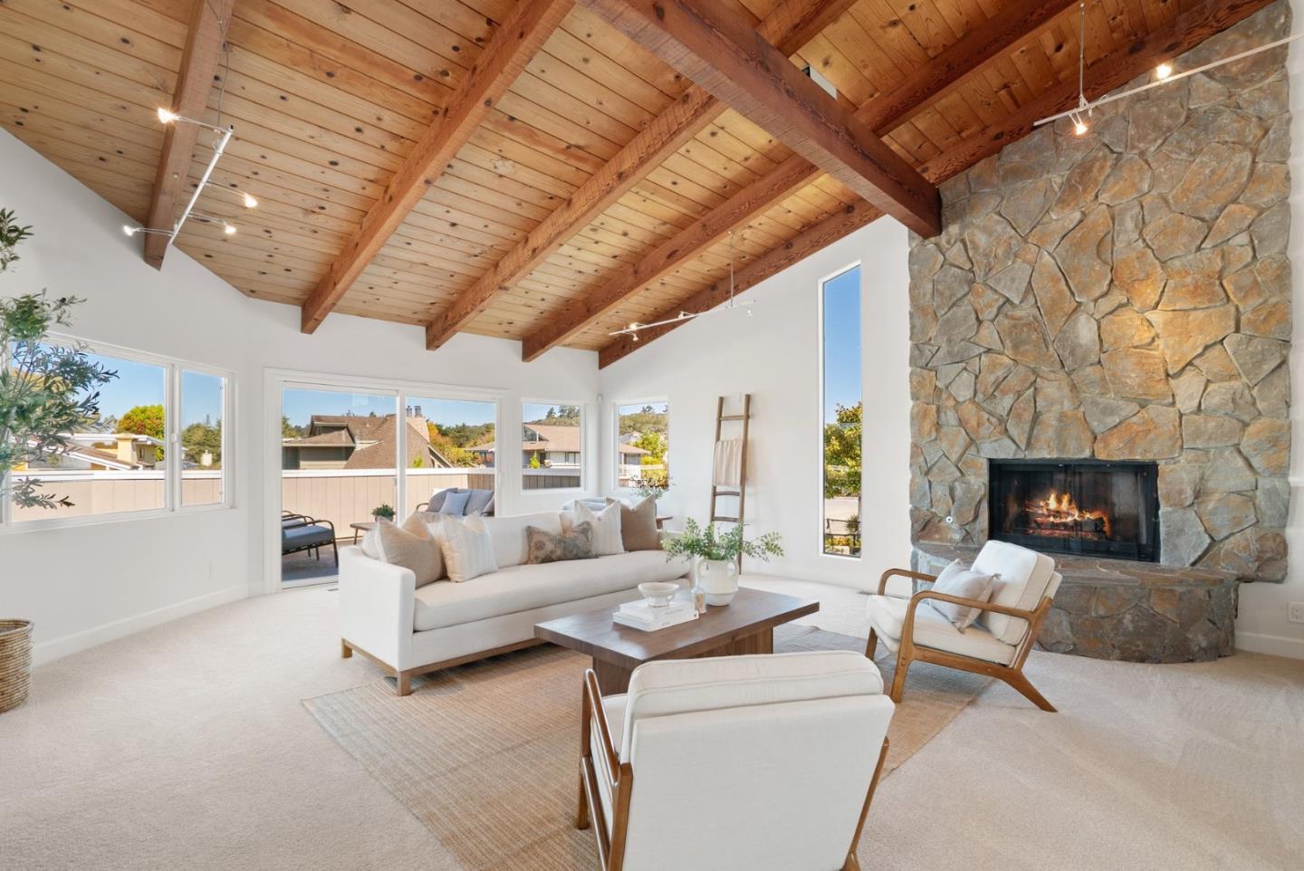 Living room with a vaulted timber ceiling, stone fireplace, and neutral seating.
