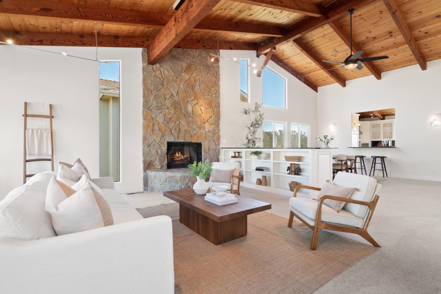 Living room with a vaulted wood ceiling, tall stone fireplace, white built-ins, and neutral seating.