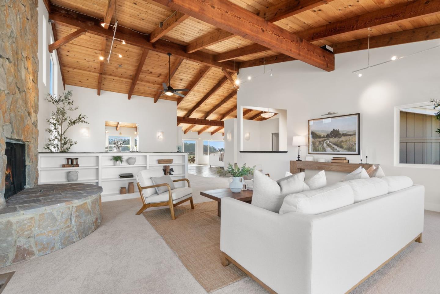 Living room with a vaulted wood-beam ceiling, stone fireplace, and white seating.