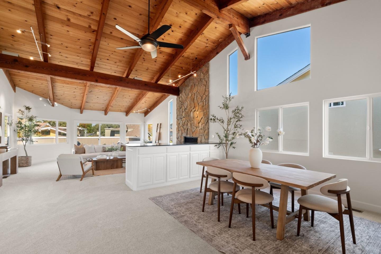 Open-plan living and dining room with vaulted wood ceiling and stone fireplace.
