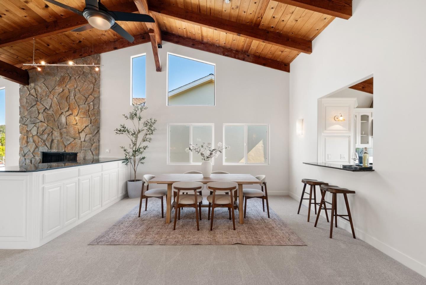 Furnished dining area with a vaulted wood ceiling, stone fireplace, and kitchen counter with bar stools.
