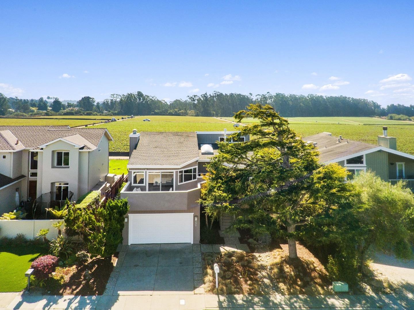 Two-story home with a garage and landscaped yard, photographed from above with open fields behind it.