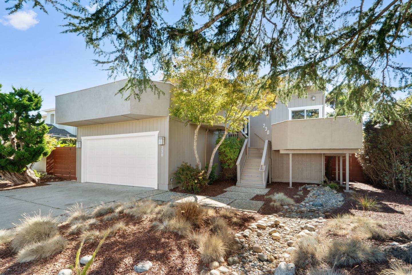 Modern two-level home with a white garage, raised entry stairs, and a landscaped dry creek bed.