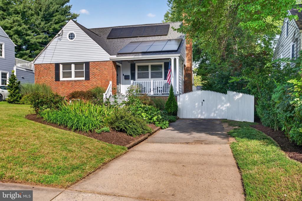 Brick-and-white house with rooftop solar panels, a front porch, and a white driveway gate.