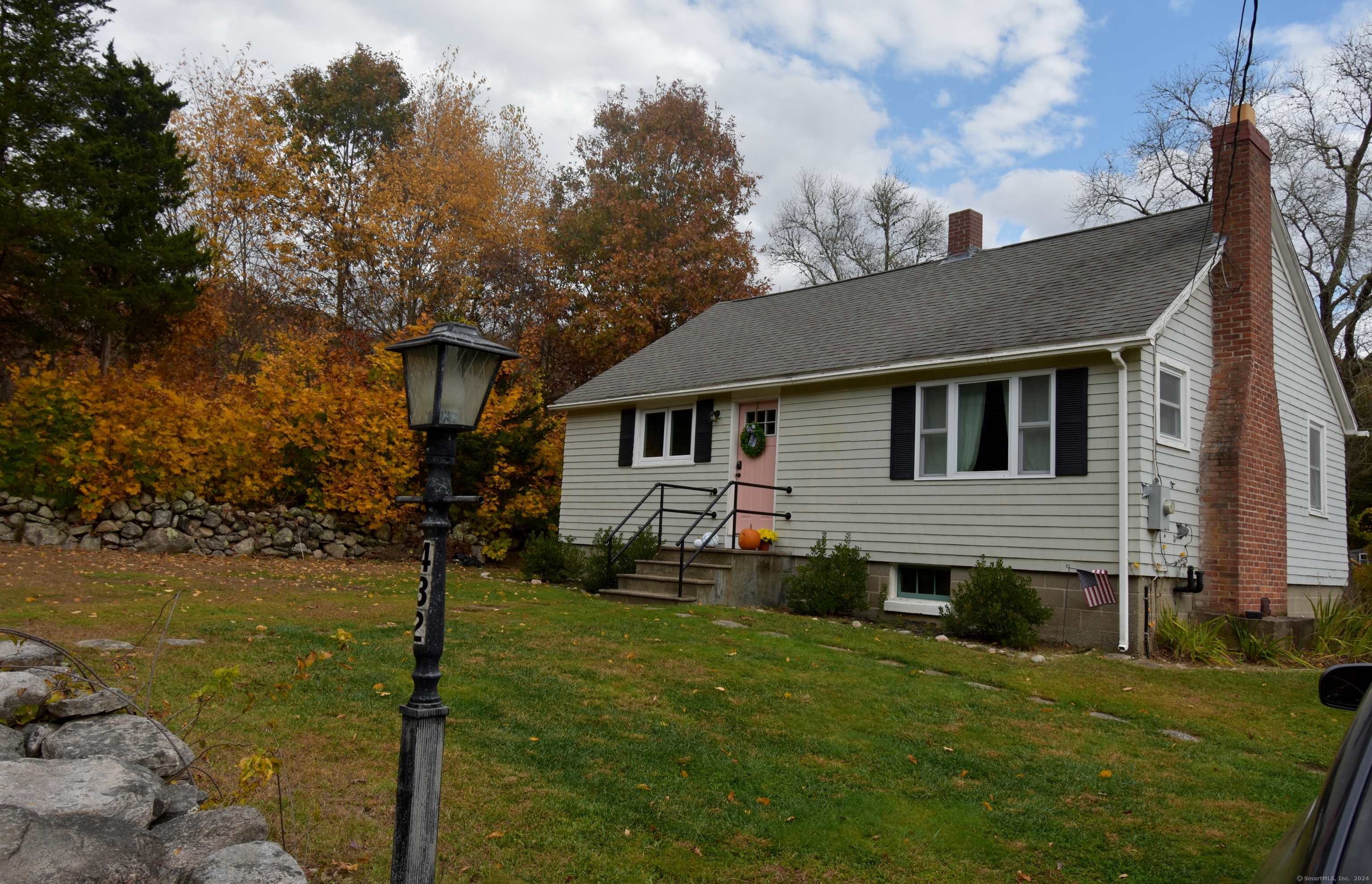 Light-sided house with a pink front door and tall brick chimney, framed by autumn trees.