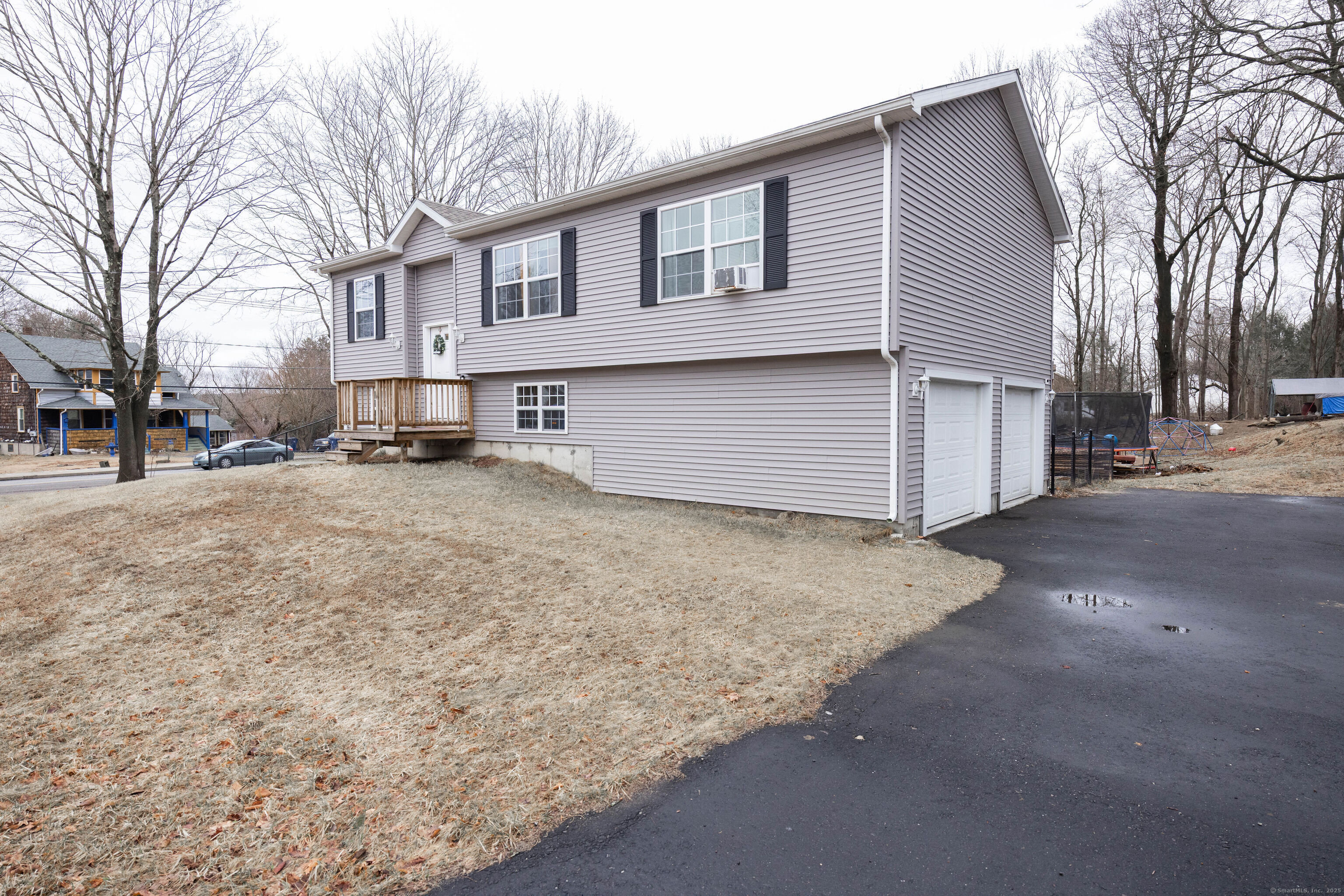 Gray raised-ranch house with a small wooden entry deck, two garage doors, and a paved driveway.