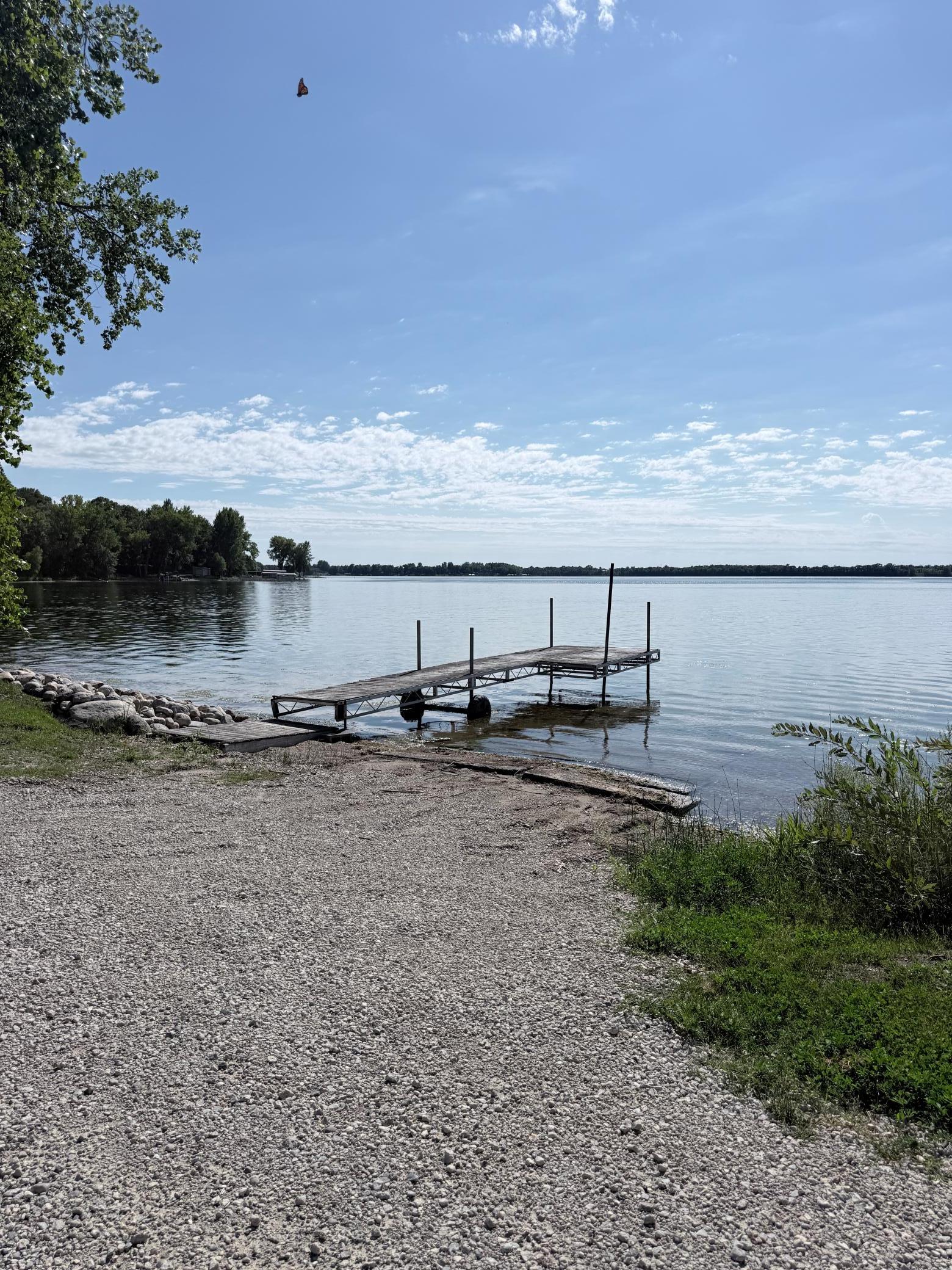 Rocky lakefront beach with a dock extending over calm water.
