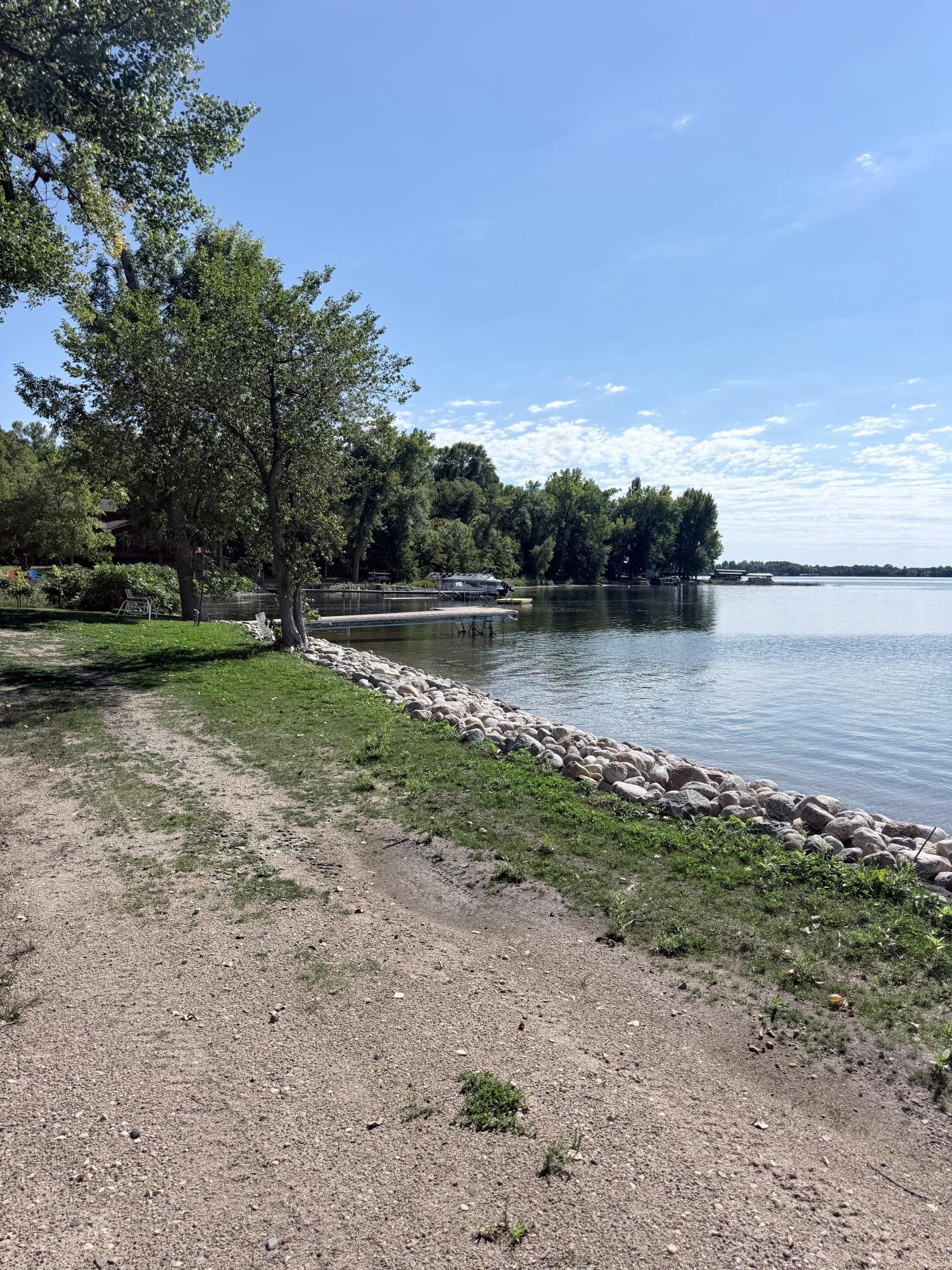 Tree-lined lakeshore with a rocky bank, private dock, and boats on the water.