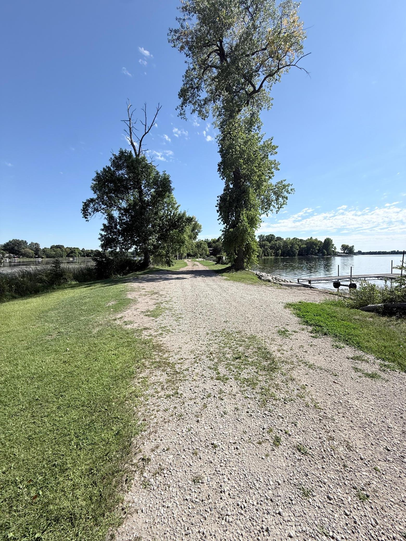 Gravel lane leads to a lakeshore dock between mature trees.