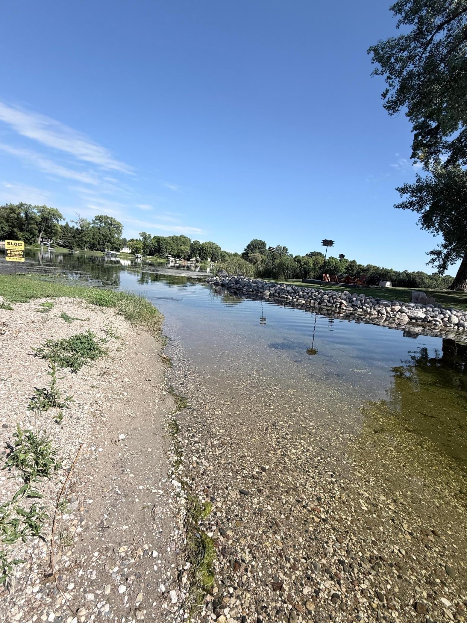 Shallow lake water meets a pebbled shore beside a stone embankment.