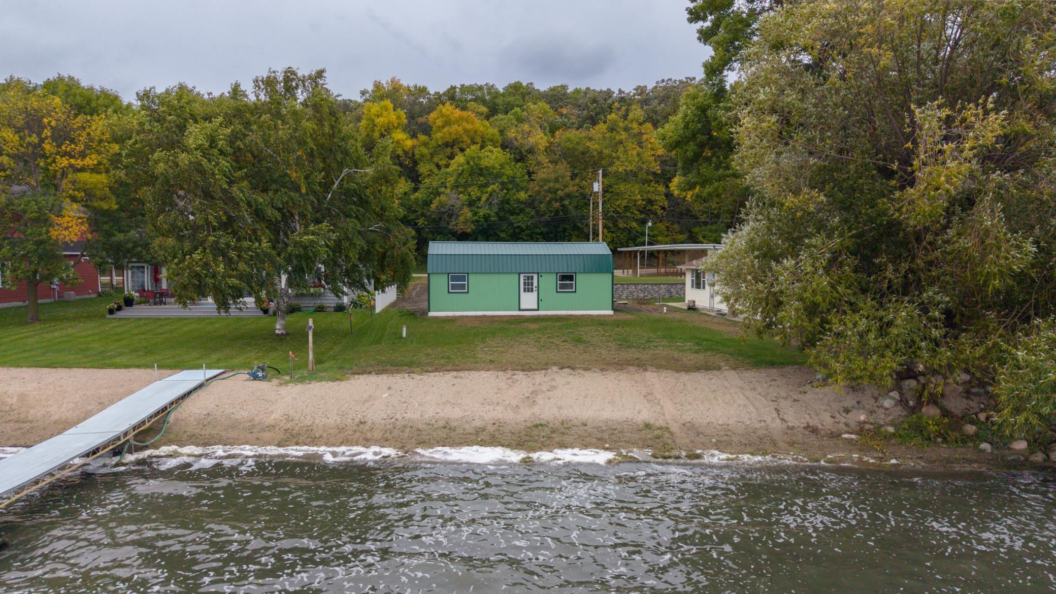 Lakefront property with a green outbuilding, sandy shore, and dock extending into the water.