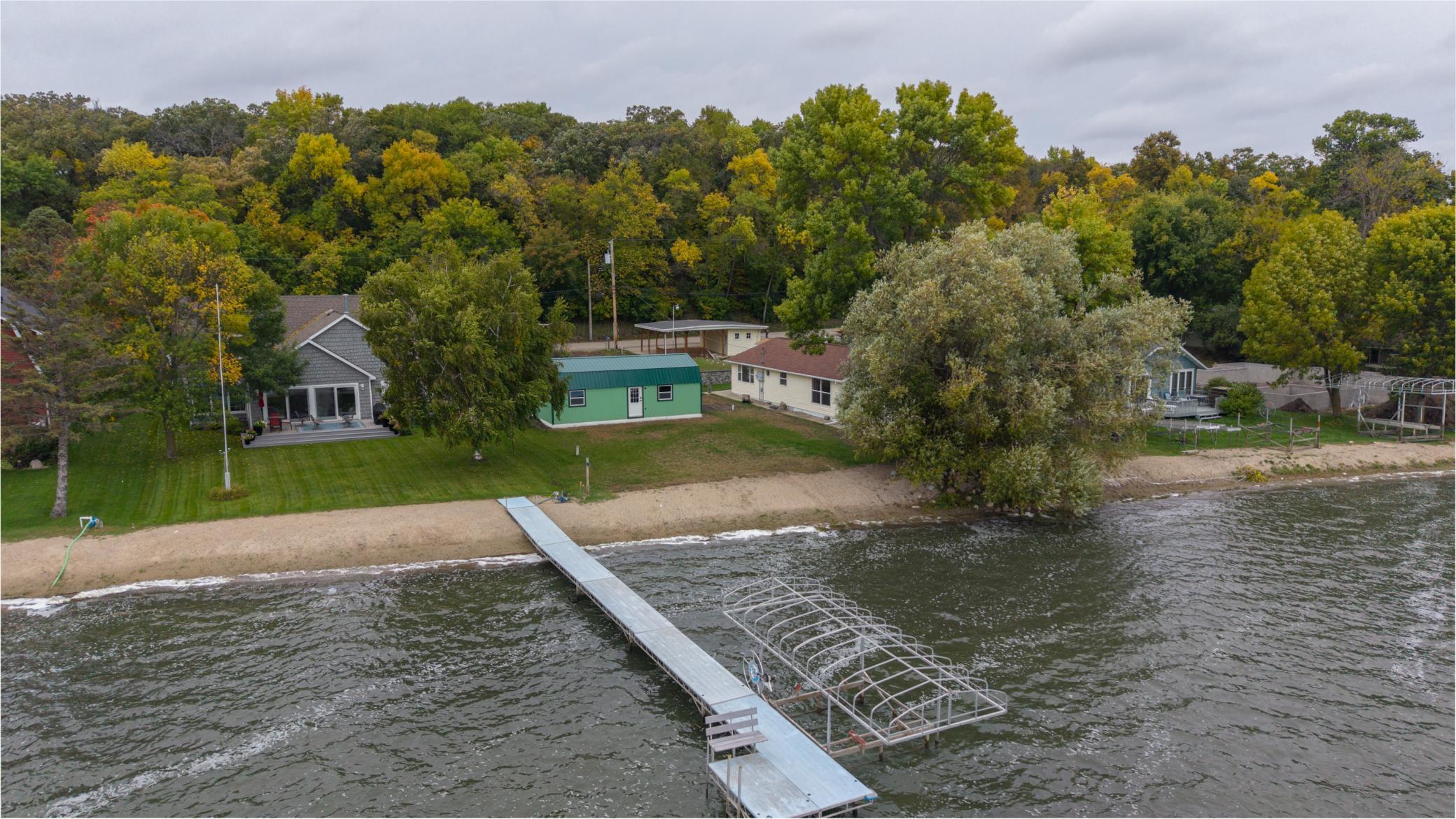Aerial view of a lakeside property with a sandy shore, long dock, and boat lift.