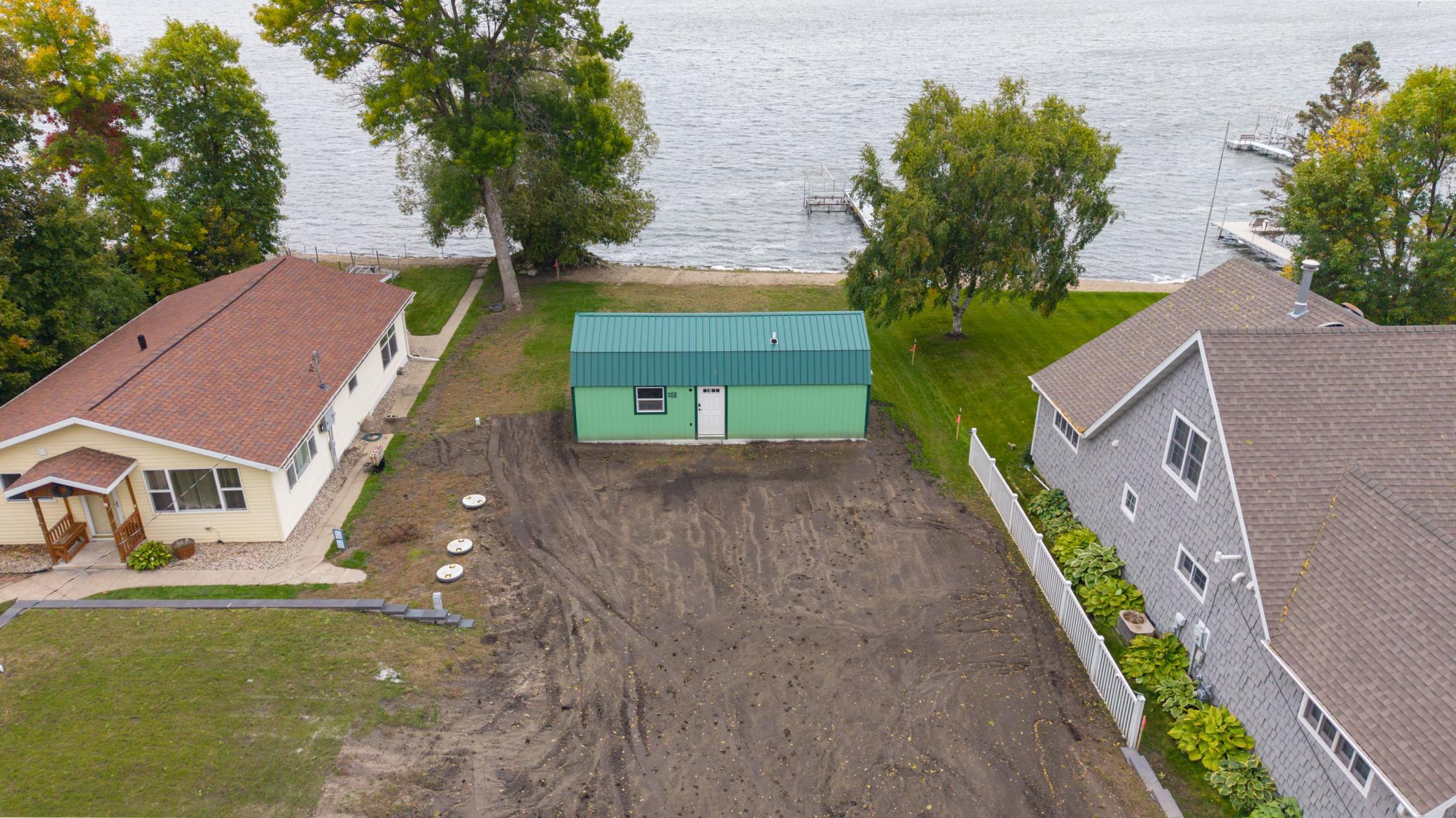Cleared lakeside lot with a green outbuilding, neighboring homes, and docks along the shore.