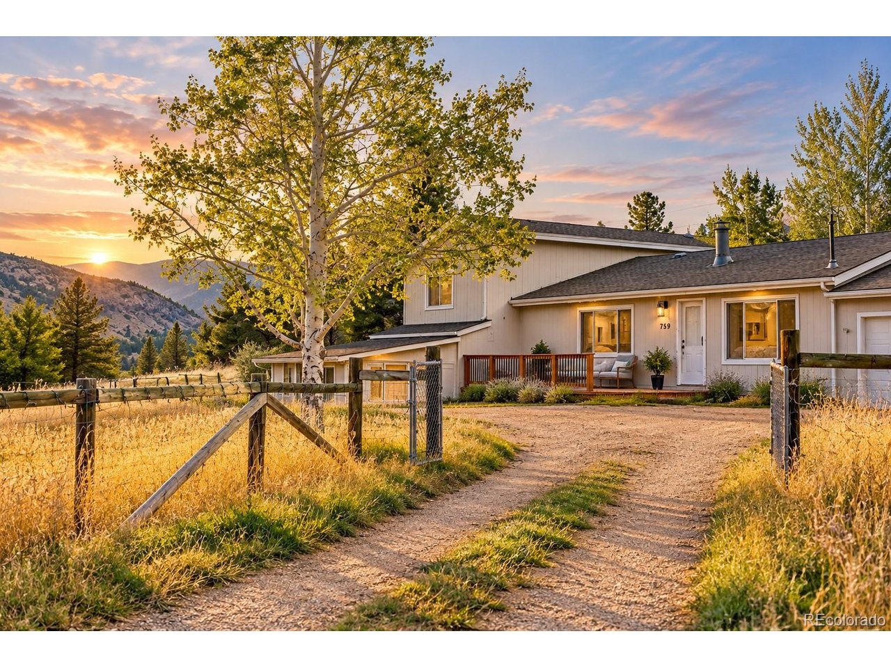 Mountain-front home with a fenced gravel drive and sunset-lit aspen trees.