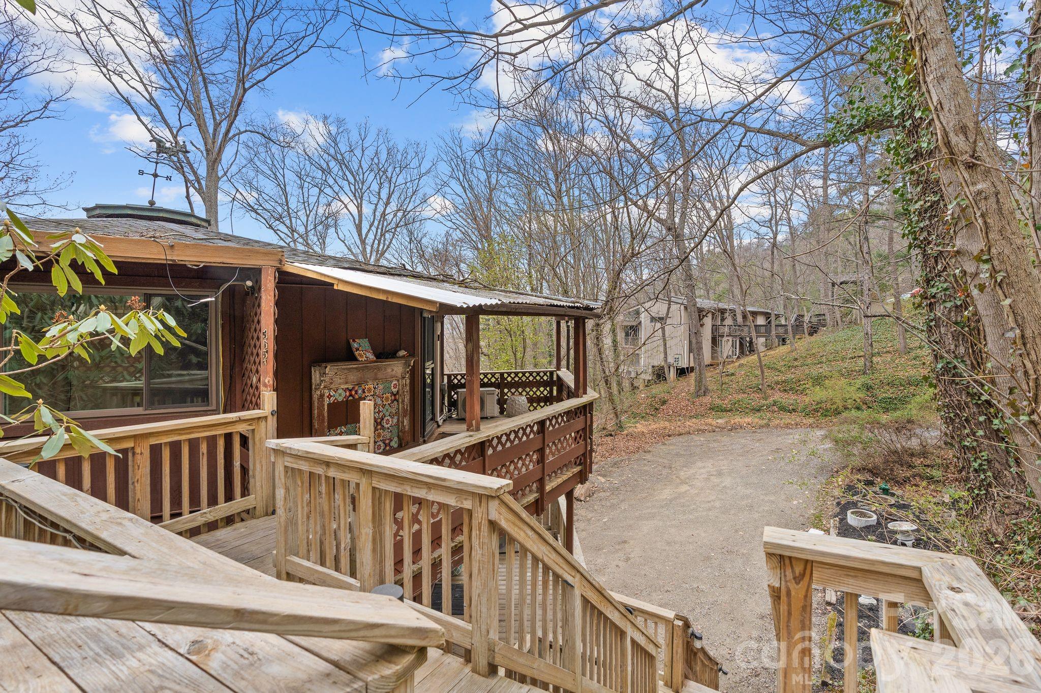 Rustic brown home with a covered wooden porch and deck stairs on a wooded hillside.