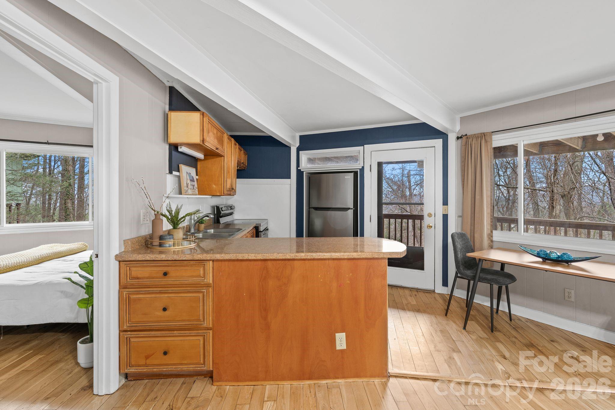 Kitchen with a wood peninsula, angled white ceiling beams, and windows overlooking leafless trees.