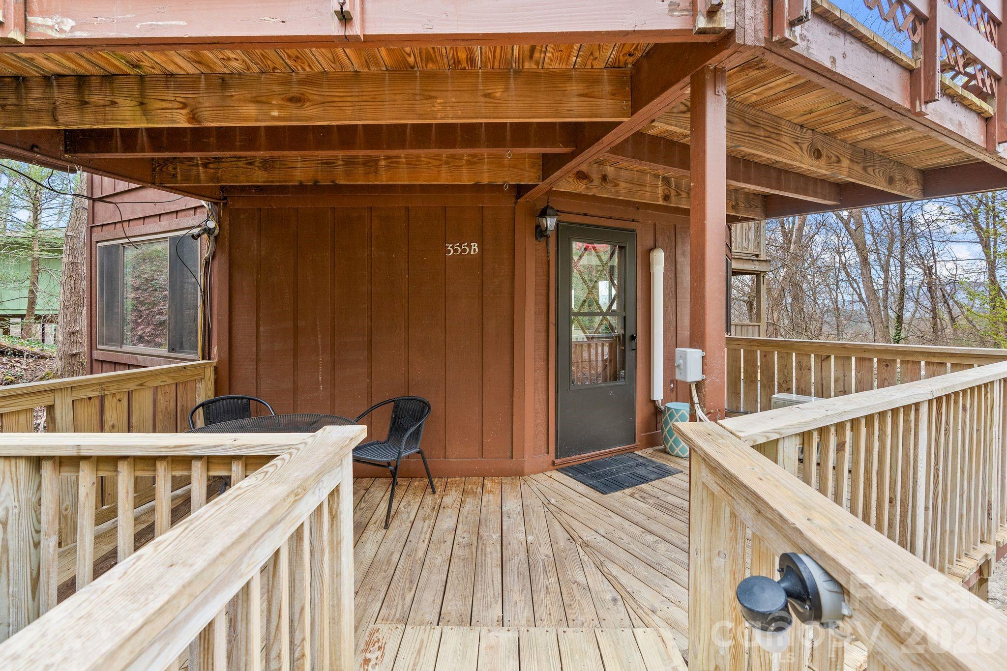 Covered wooden porch with light railings, two black chairs, and a dark screen door.