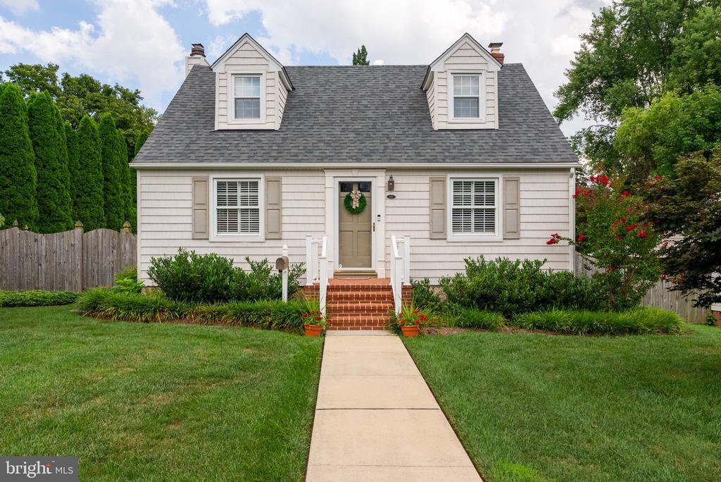 Light-colored Cape Cod home with twin dormers, brick steps, and a walkway through the lawn.