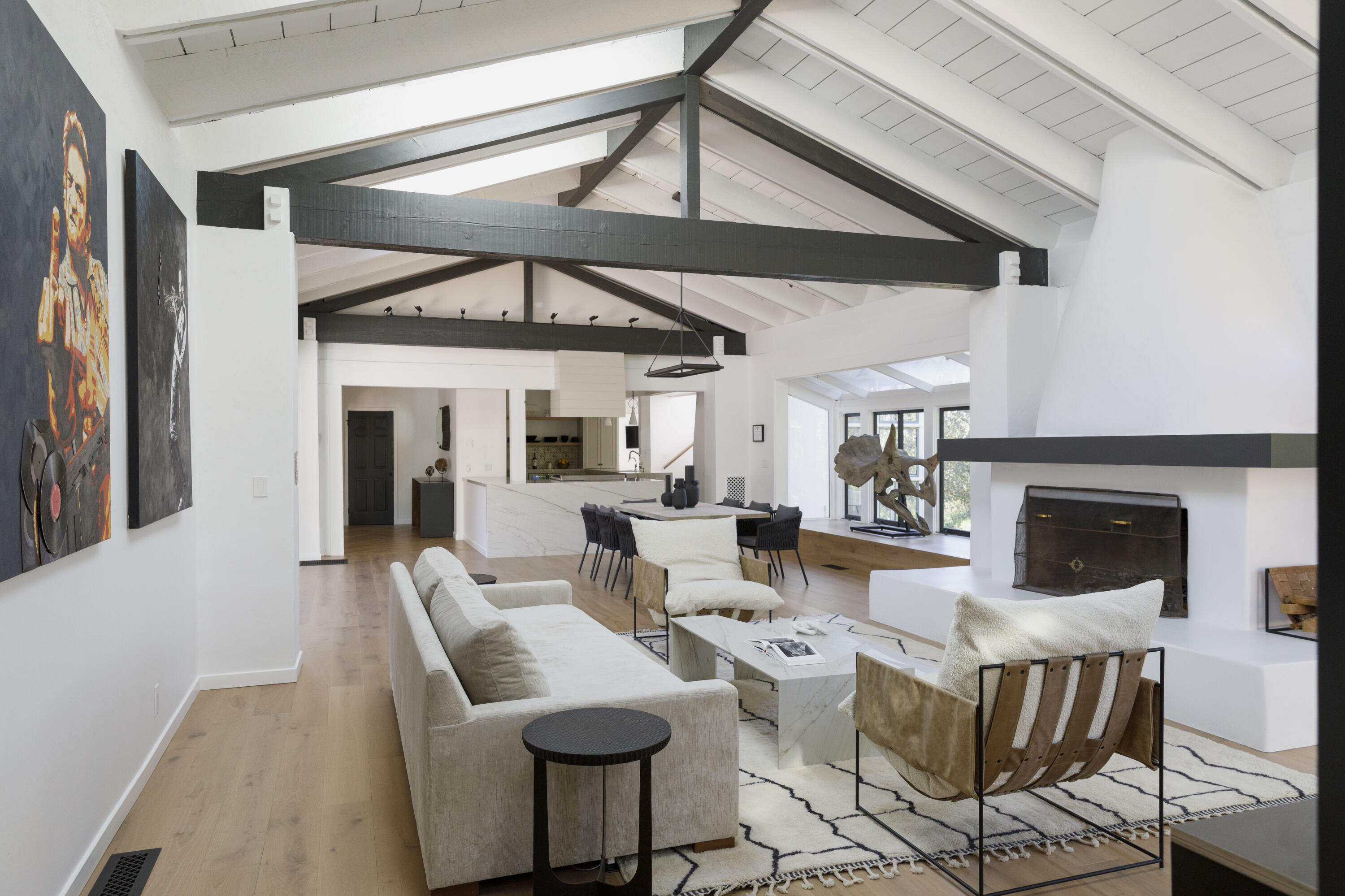 Vaulted living room with exposed beams, contemporary seating, fireplace, and adjoining kitchen and dining area.