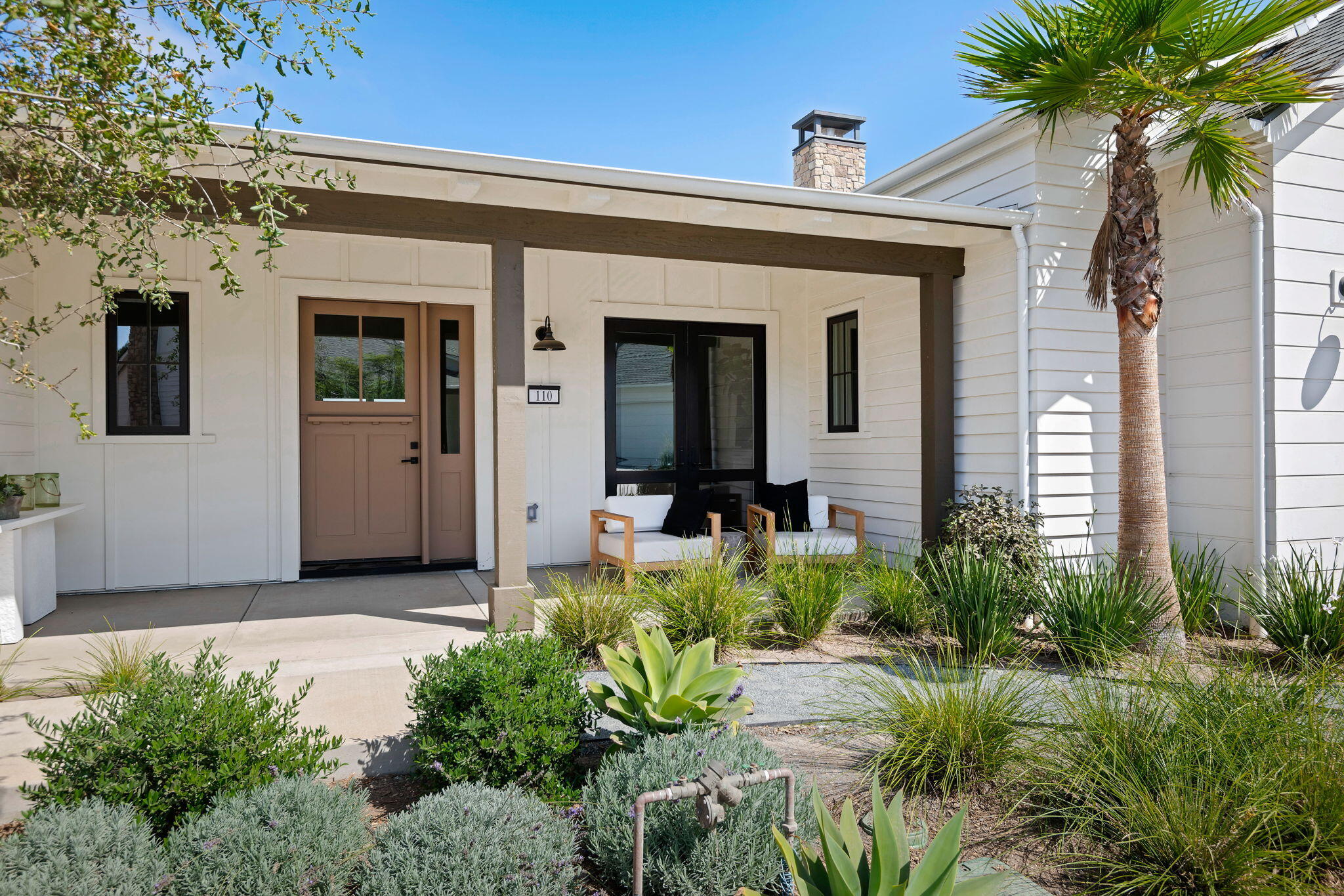 White home with a covered porch, taupe entry door, outdoor seating, and landscaped front yard.