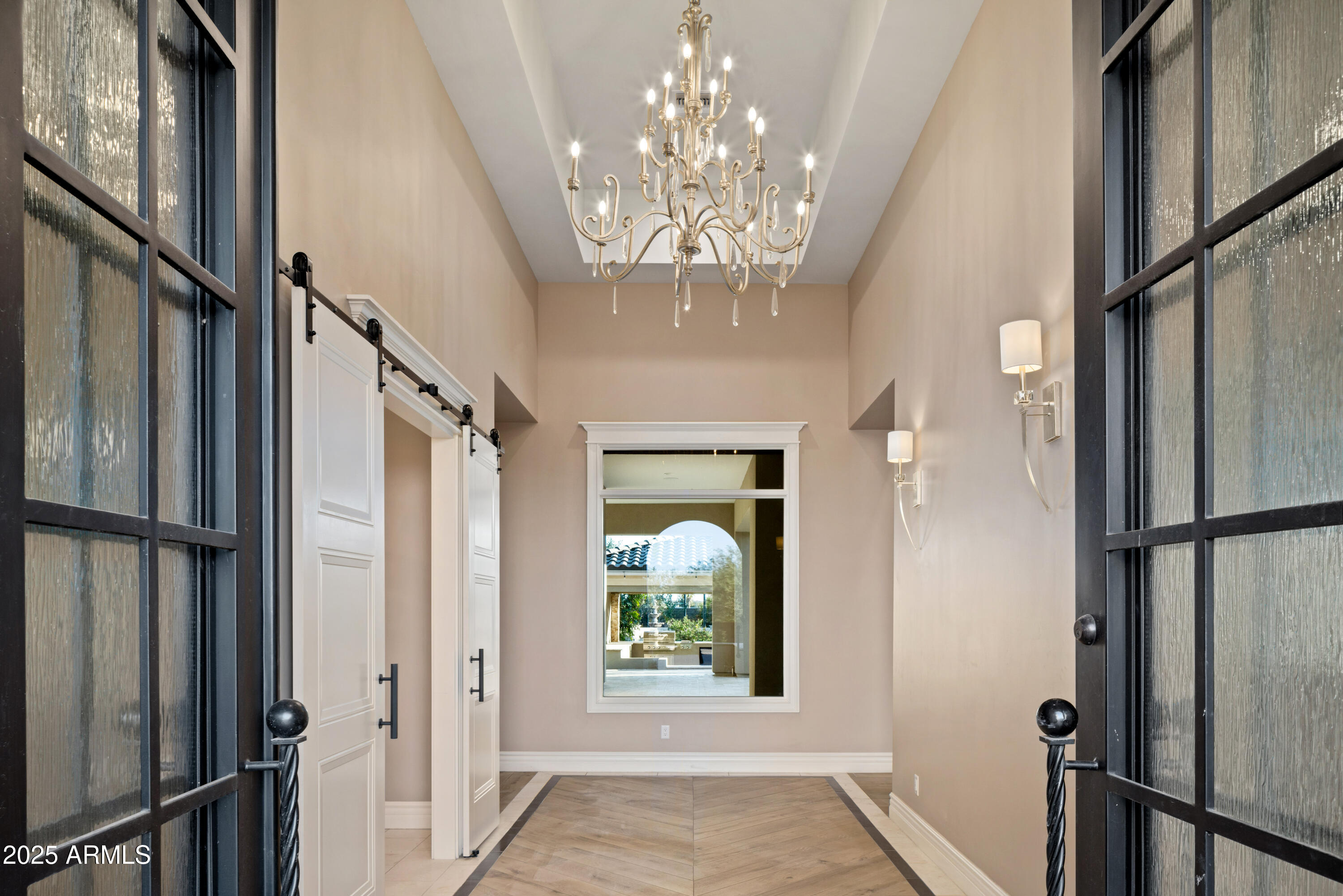 High-ceilinged entry foyer with a chandelier, black-framed glass doors, and patterned tile flooring.