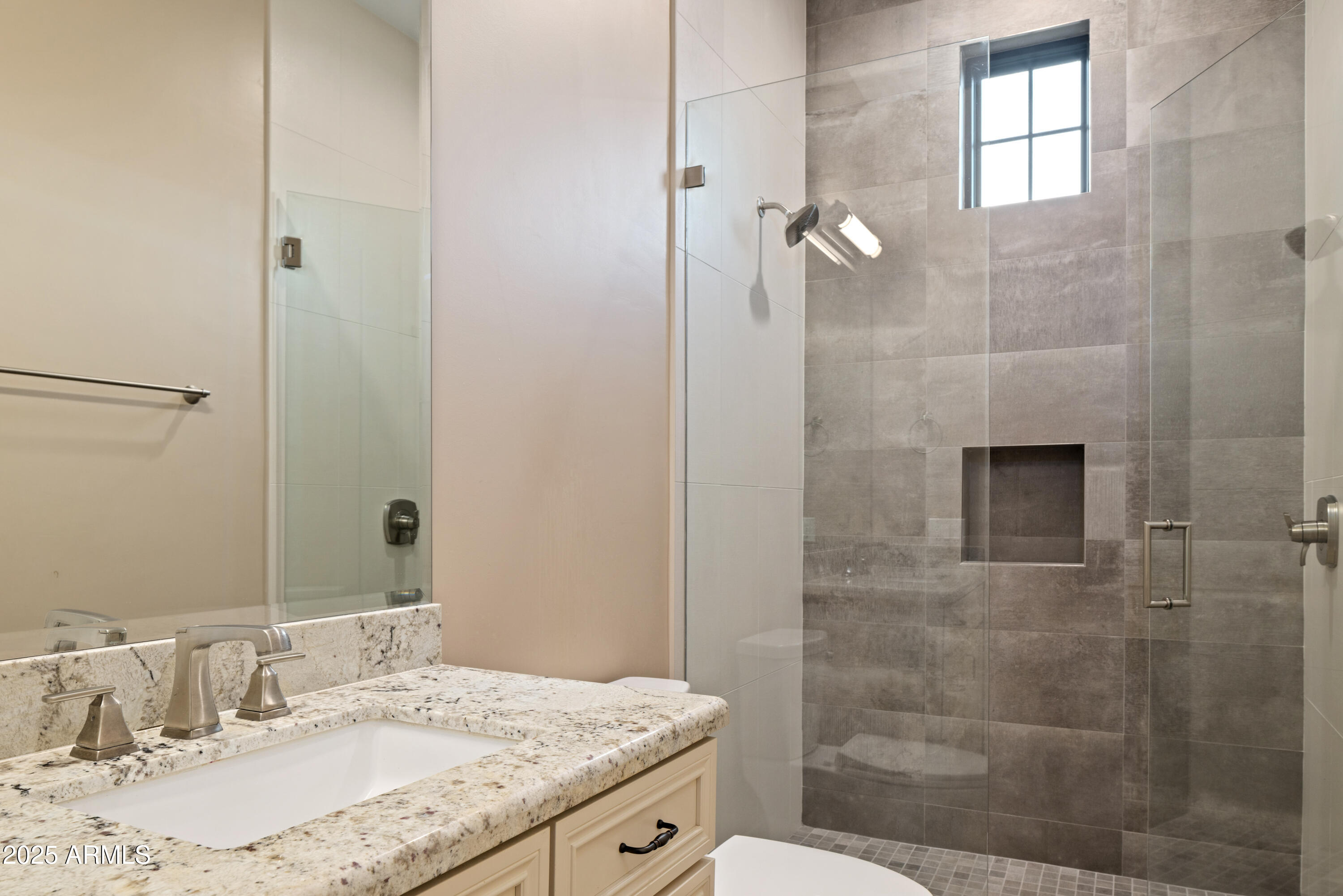 Bathroom with granite vanity and glass-enclosed gray tile shower with a high window.