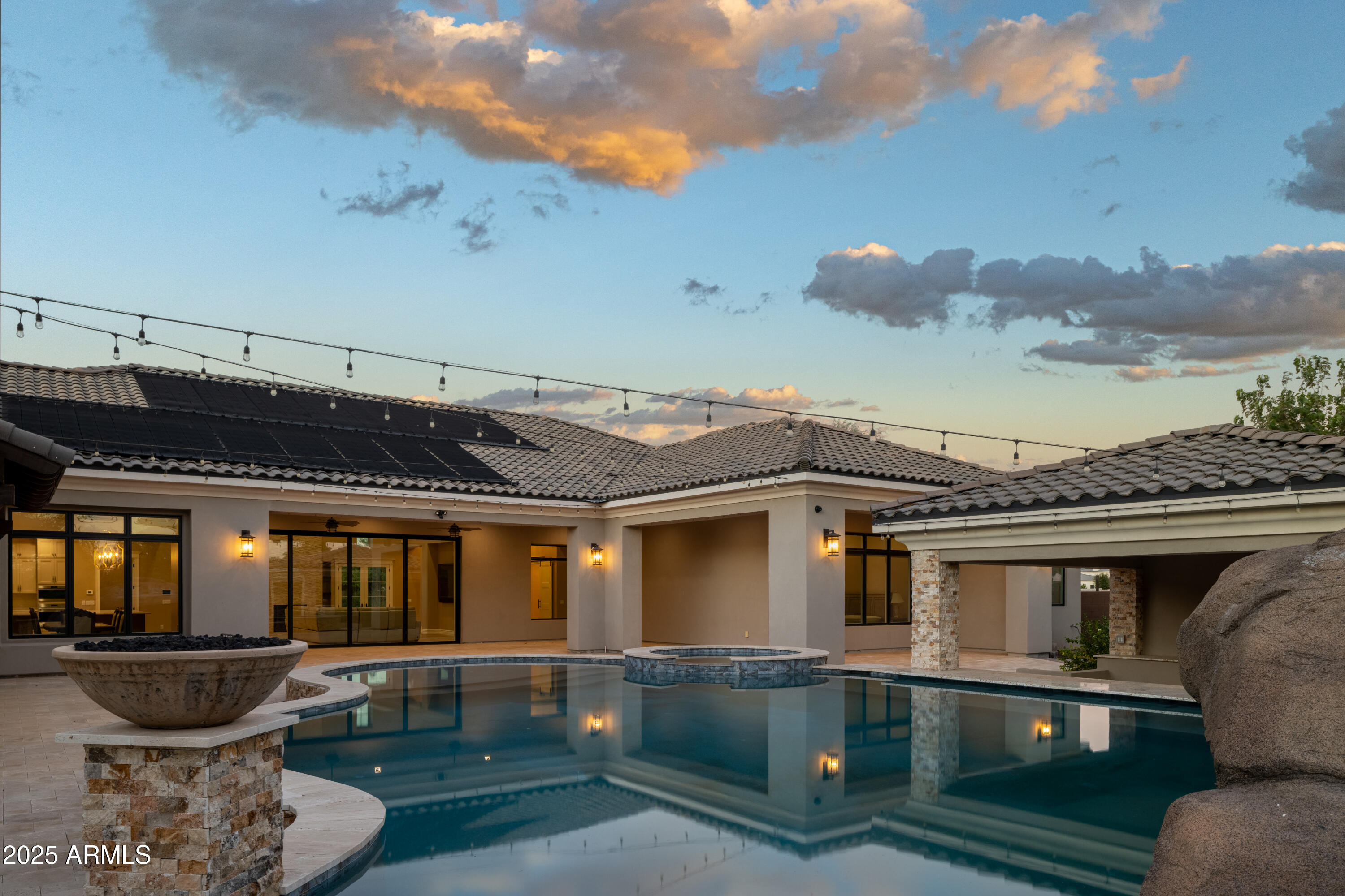 Home’s rear patio and pool at dusk, with a raised spa and solar panels on the roof.