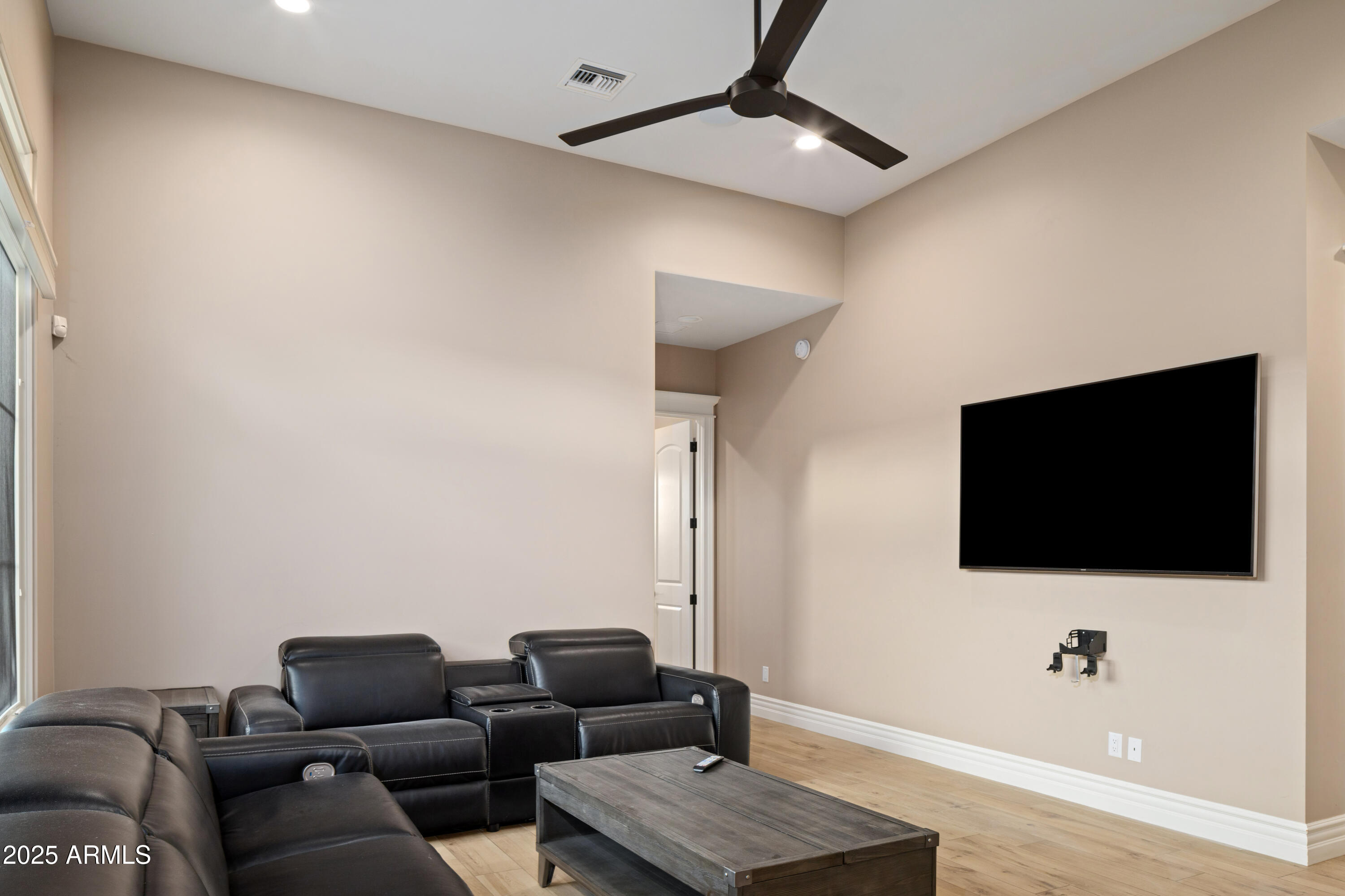 Media room with black leather recliners, wall-mounted television, and wood coffee table.