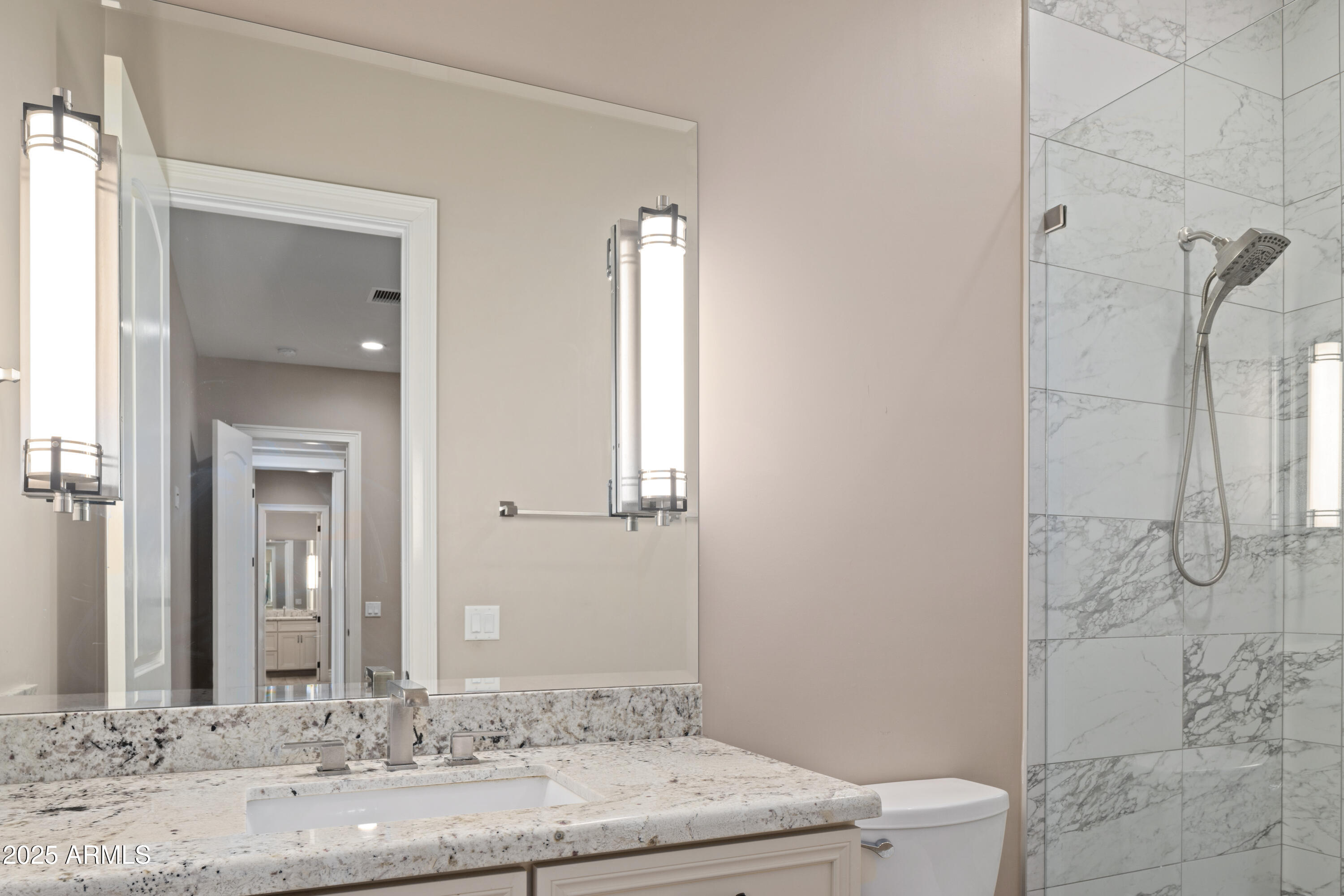 Bathroom vanity with granite countertop and mirror beside a marble-look tiled walk-in shower.