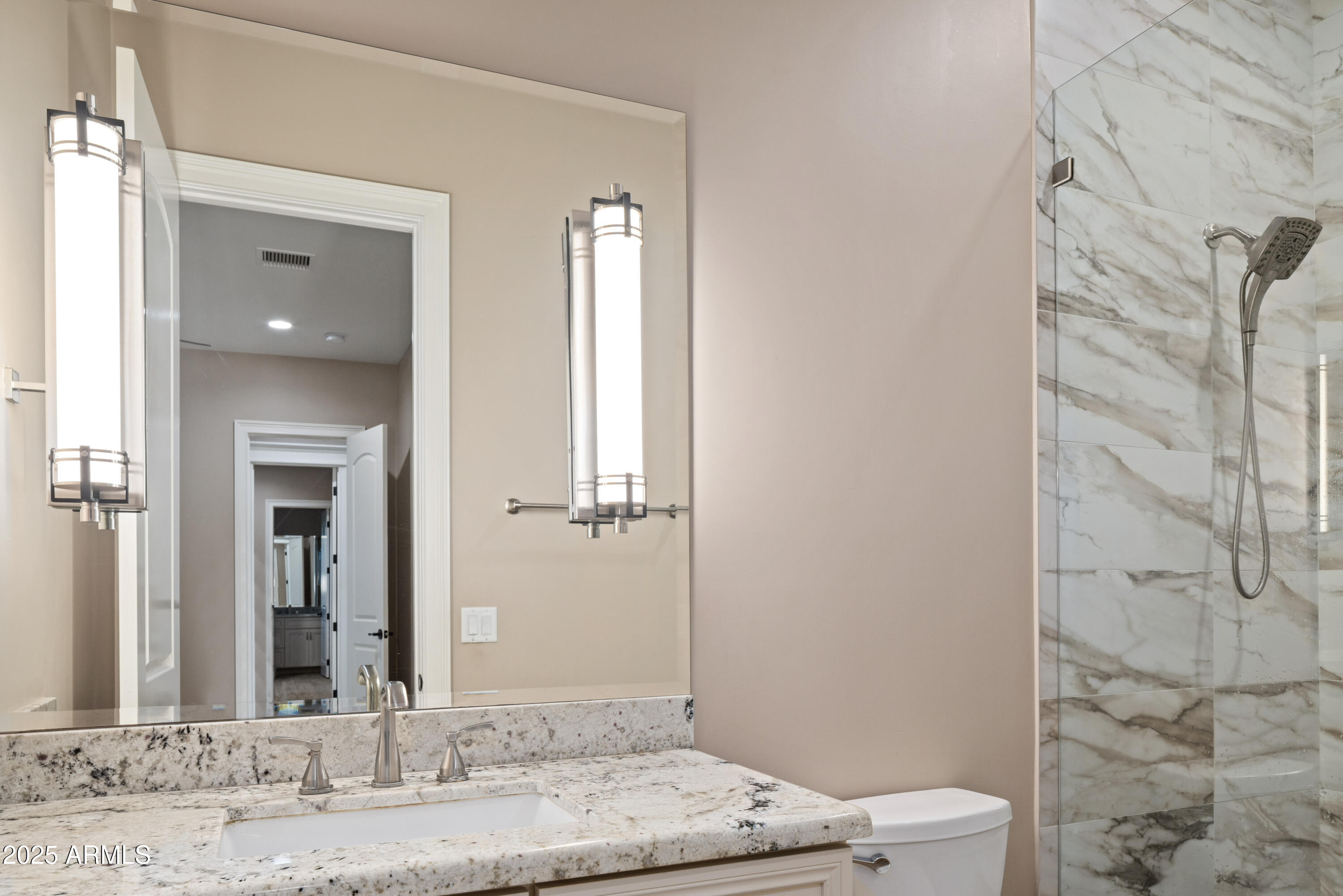 Bathroom vanity with granite countertop and mirror beside a marble-look tiled shower.