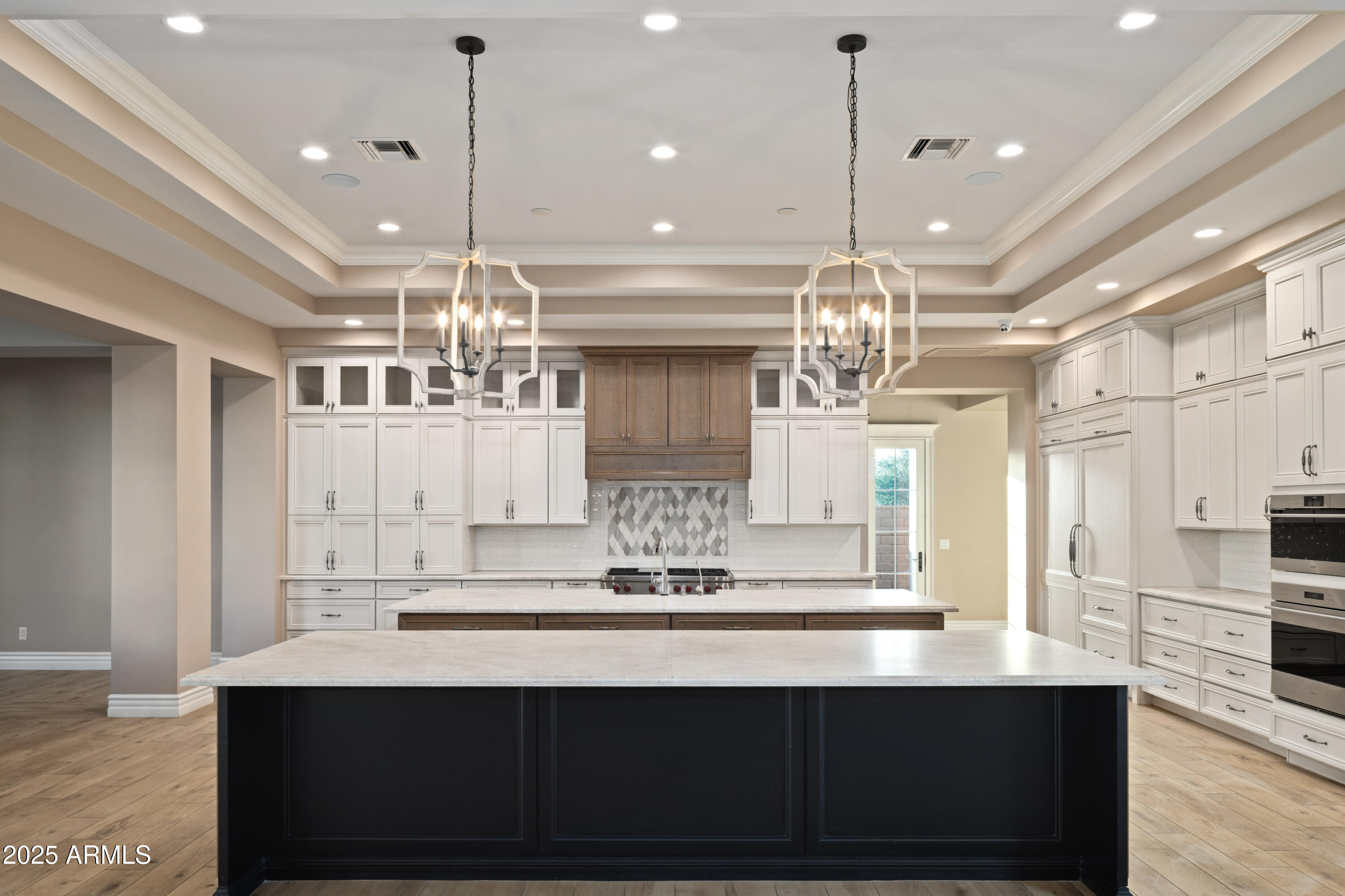 Spacious kitchen with a large dark island, white cabinets, patterned backsplash, and twin pendant chandeliers.