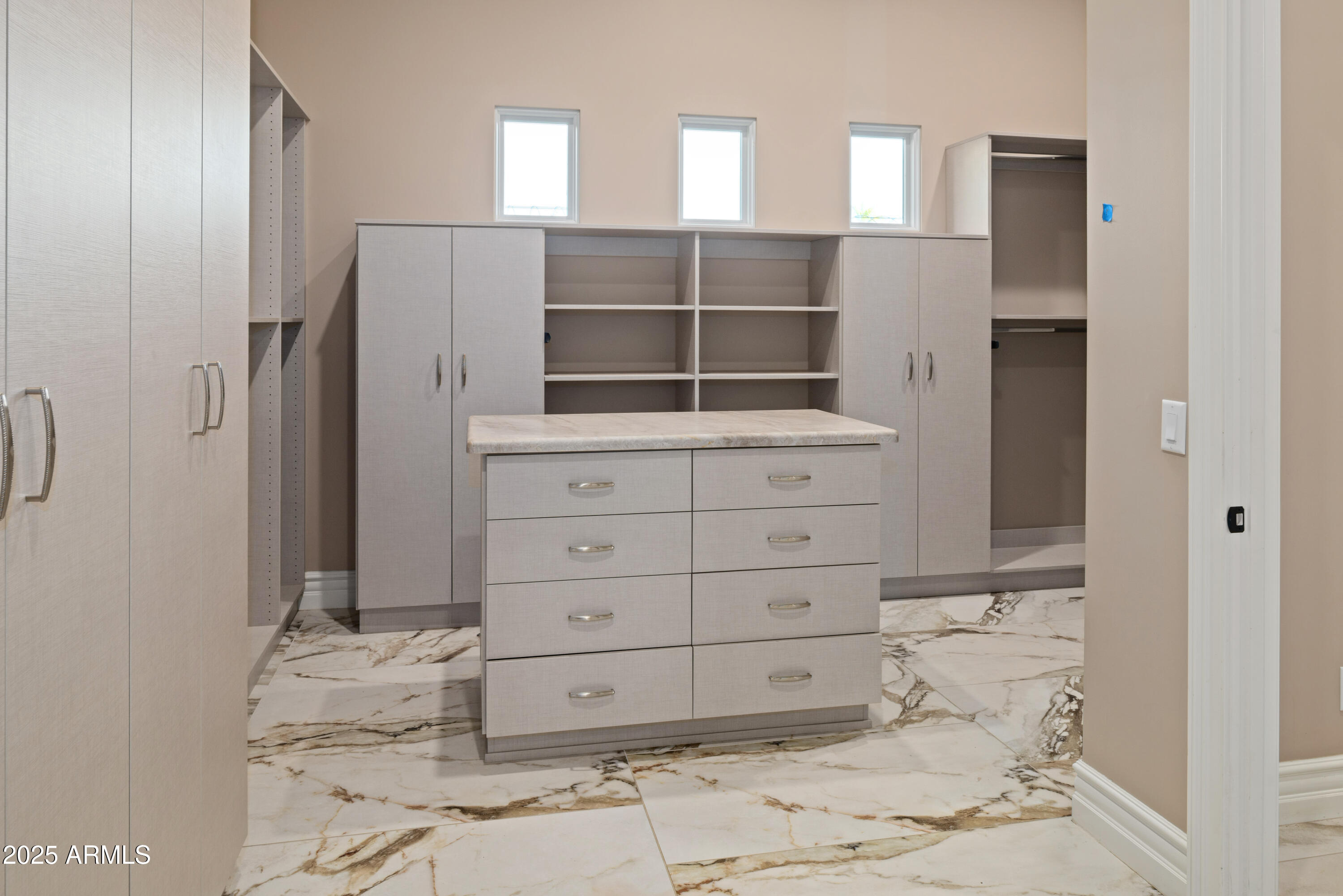 Walk-in closet with built-in cabinetry, open shelving, a central drawer island, and marble-look tile flooring.