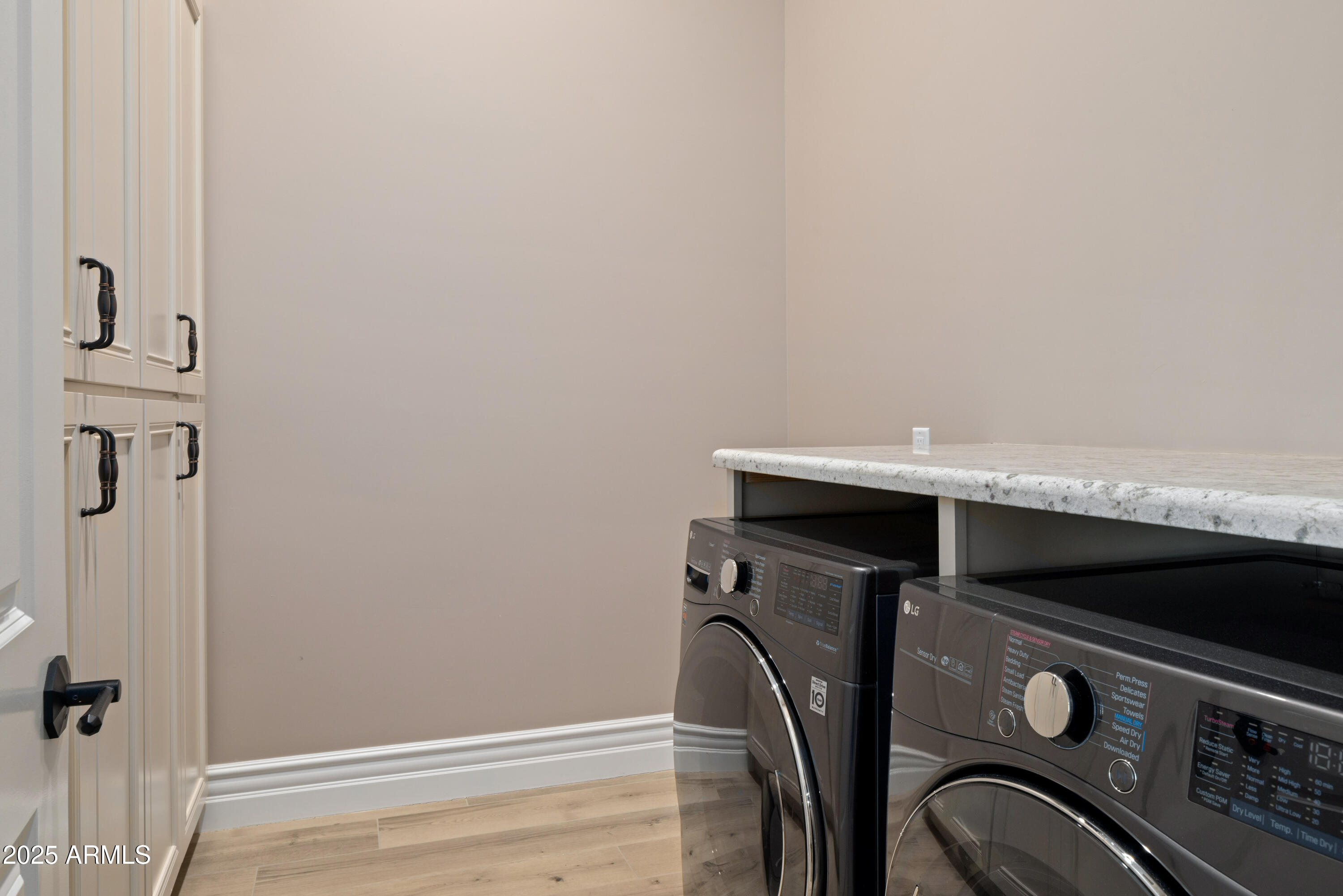 Laundry room with front-loading washer and dryer, granite countertop, and tall white cabinets.
