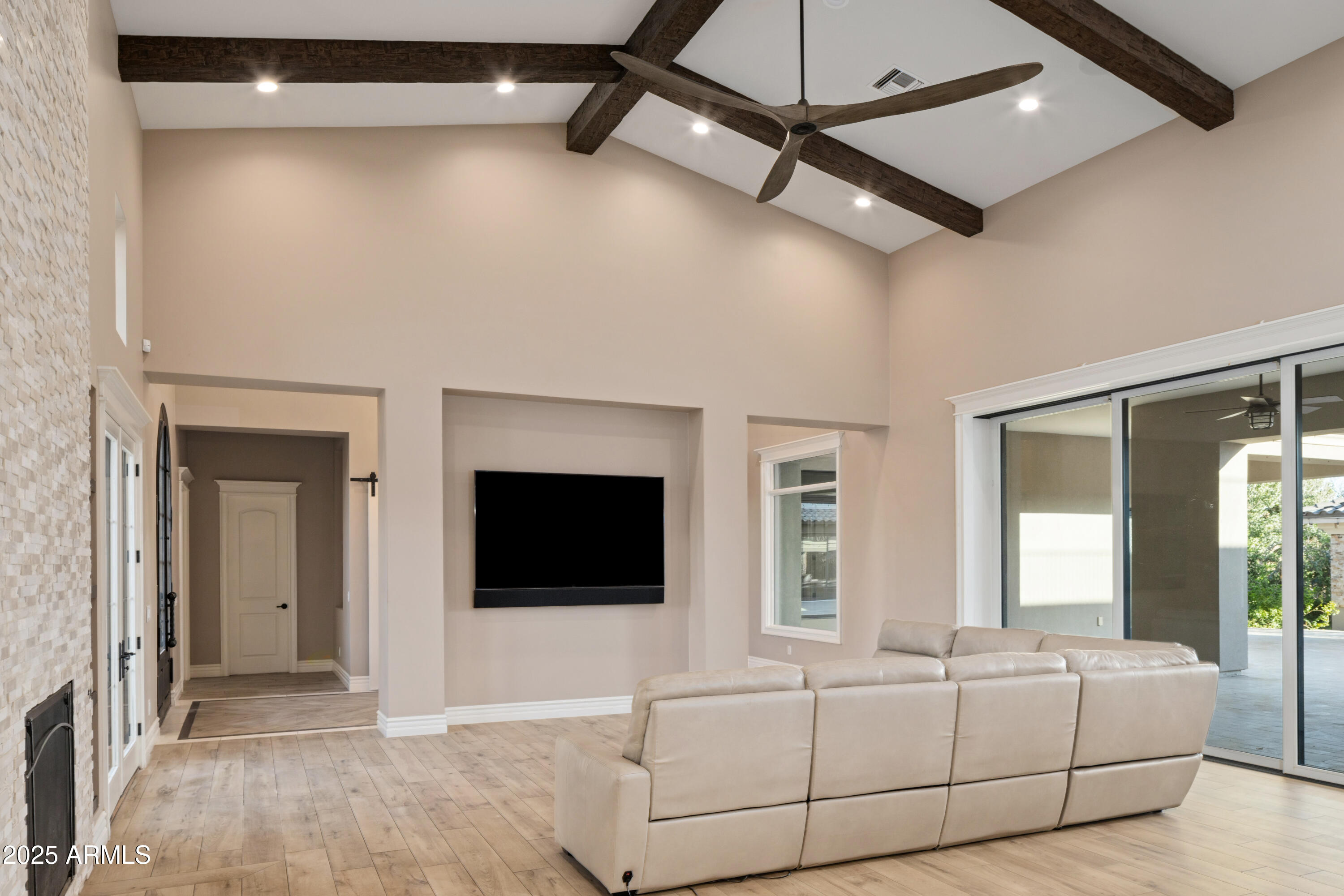 Living room with vaulted beamed ceiling, stone fireplace, sectional sofa, and sliding glass doors.